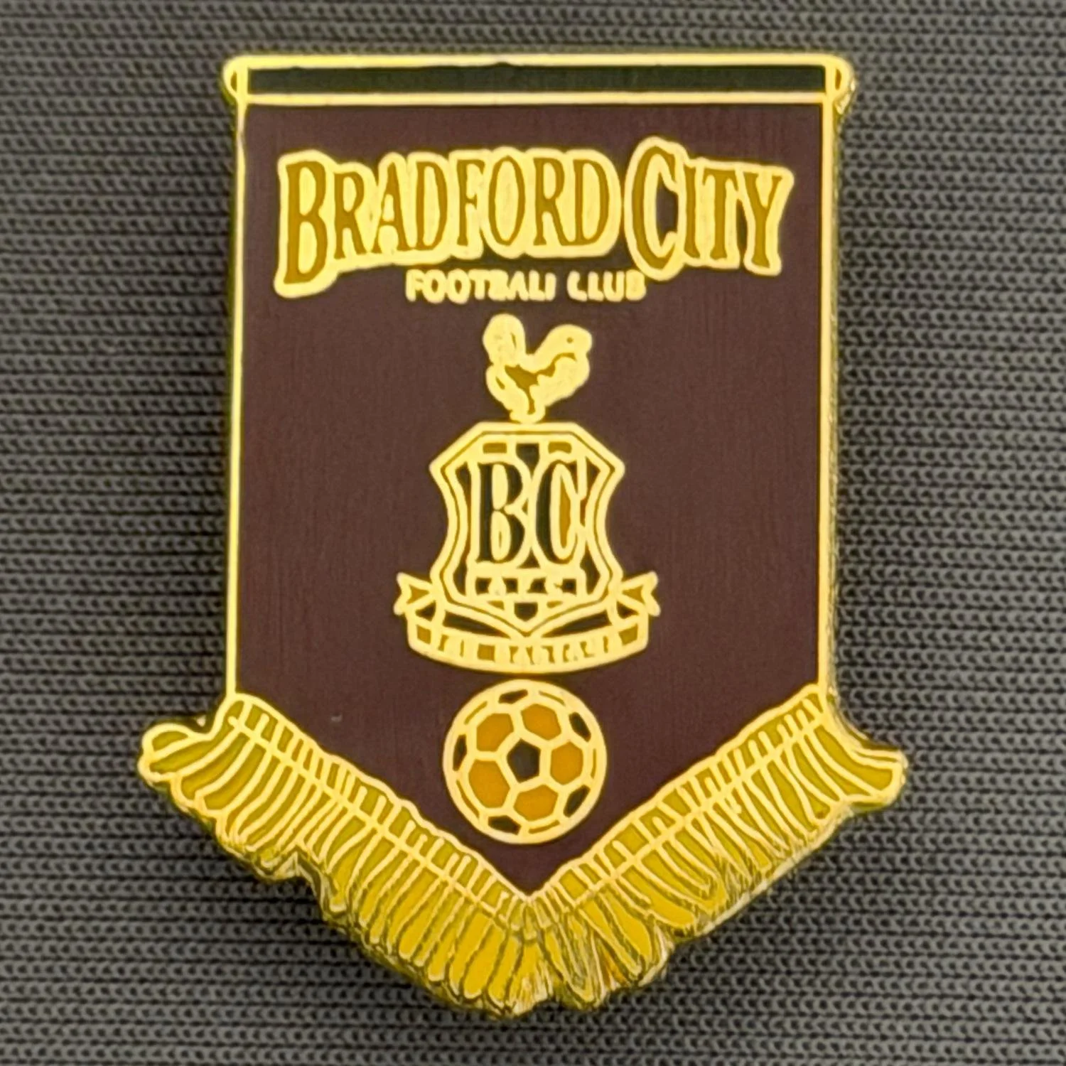 Reference Number: BCBCFC060
Size: H 28.1 mm x W 22.1 mm
Pin Type: Brooch Pin
Plating: Gold
Value: £6
Manufacturer: Andy Stokes
Comments: Claret & Amber Bradford City Pennant