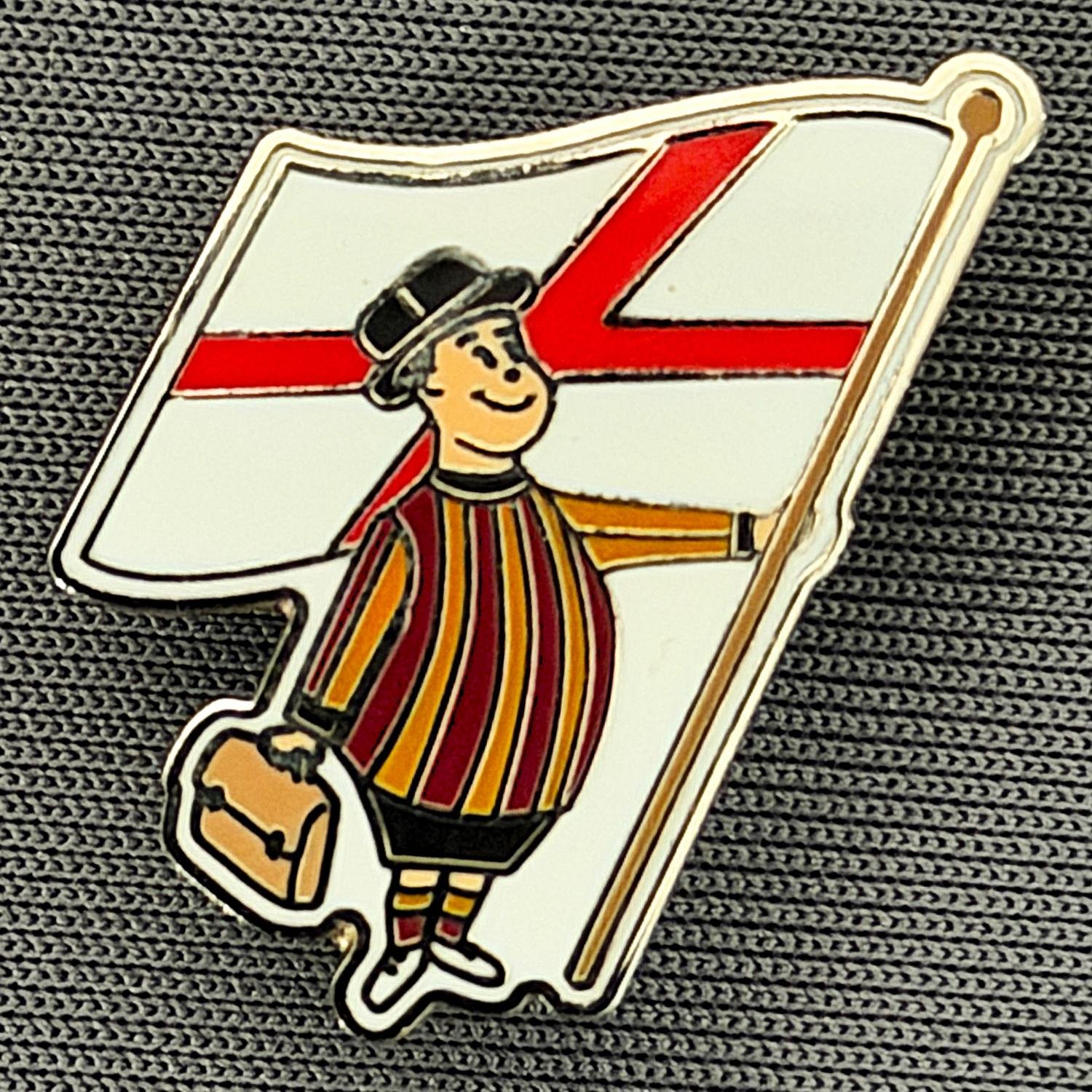 A cartoon character dressed in traditional British attire holding a flag with the Union Jack design, wearing a bowler hat, striped shirt, and carrying a satchel.