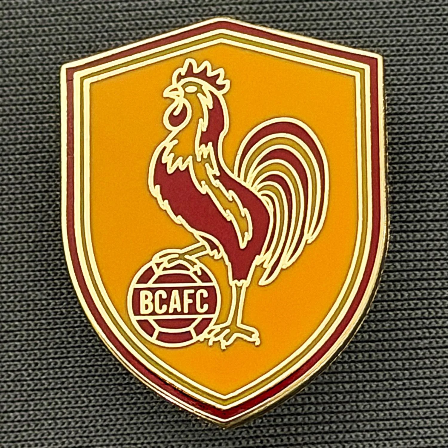 Reference Number: BCBAN083
Size: H 24.5 mm x W 19.3 mm
Pin Type: Brooch Pin
Plating: Gold
Value: £4
Manufacturer: Guy Badge Stall
Comments: Claret & Amber Bantam Ball Shield 2026