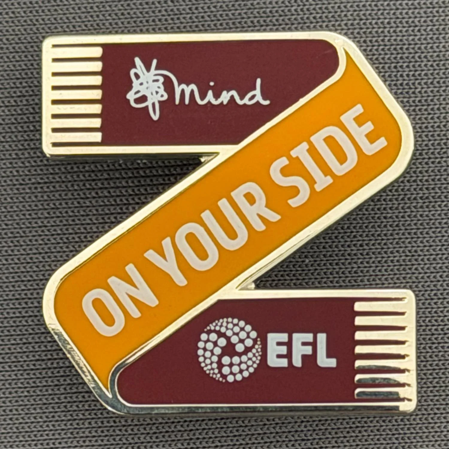Reference Number: BCSCA009
Size: H 25 mm x W 25 mm
Pin Type: Metal Clutch
Plating: Silver
Value: £6
Manufacturer: Mind Charity
Comments: Claret & Amber Scarf, Mind, EFL