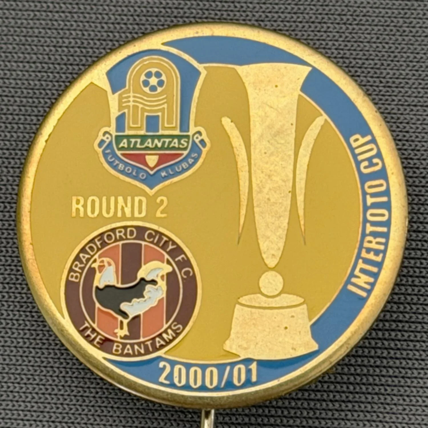Reference Number: BCRUS038
Size: D 25 mm 
Pin Type: Metal Stick Pin
Plating: Gold
Value: £12
Manufacturer: Unknown
Comments: FK Atlantas Inter Toto Cup, City Logo, Yellow & Blue Version