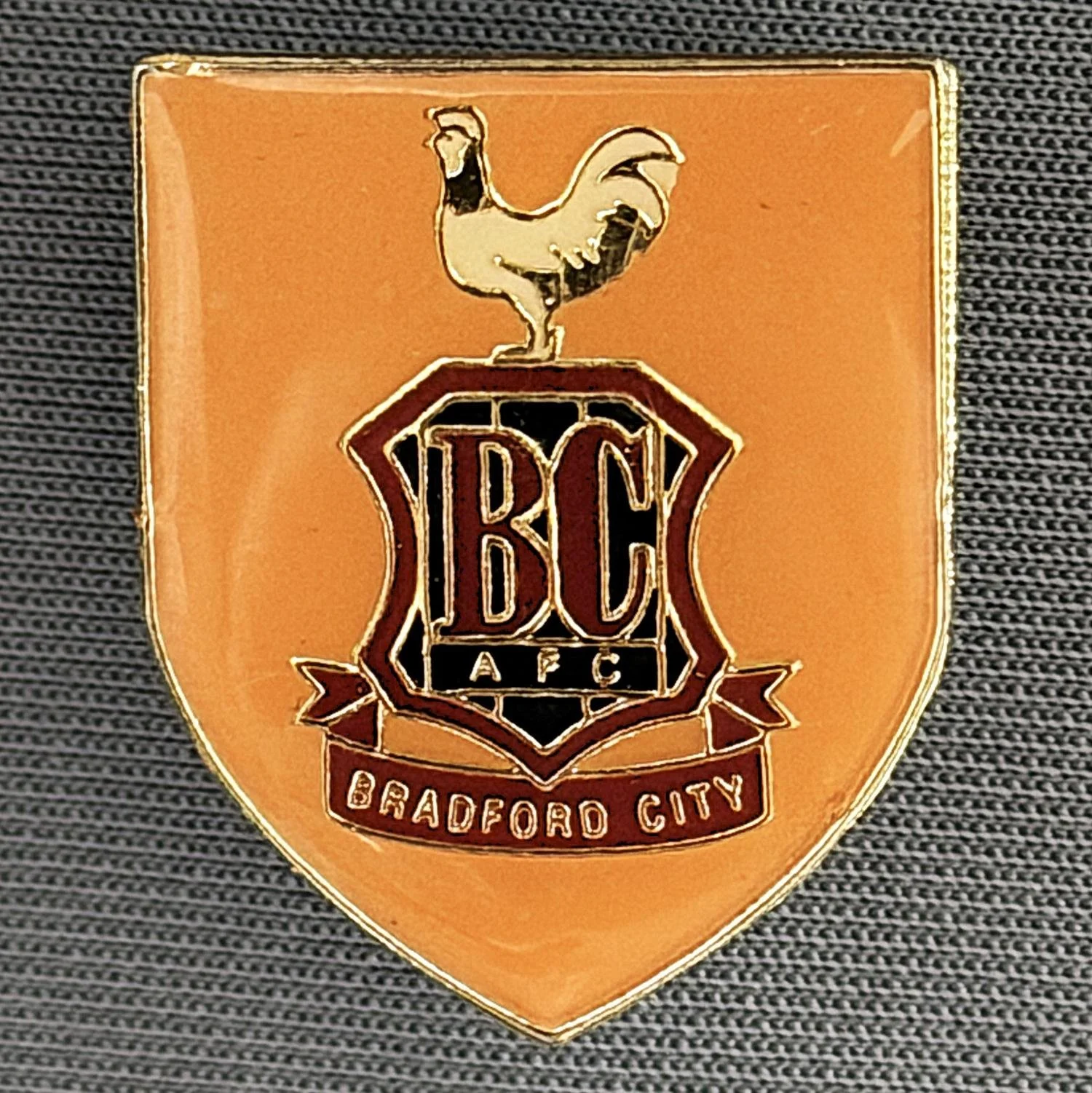 Reference Number: BCC&L014
Size: H 24.2 mm x W 19.8 mm
Pin Type: Metal Clutch
Plating: Gold
Value: £8
Manufacturer: Unknown
Comments: Amber Plastic Dome City  Logo