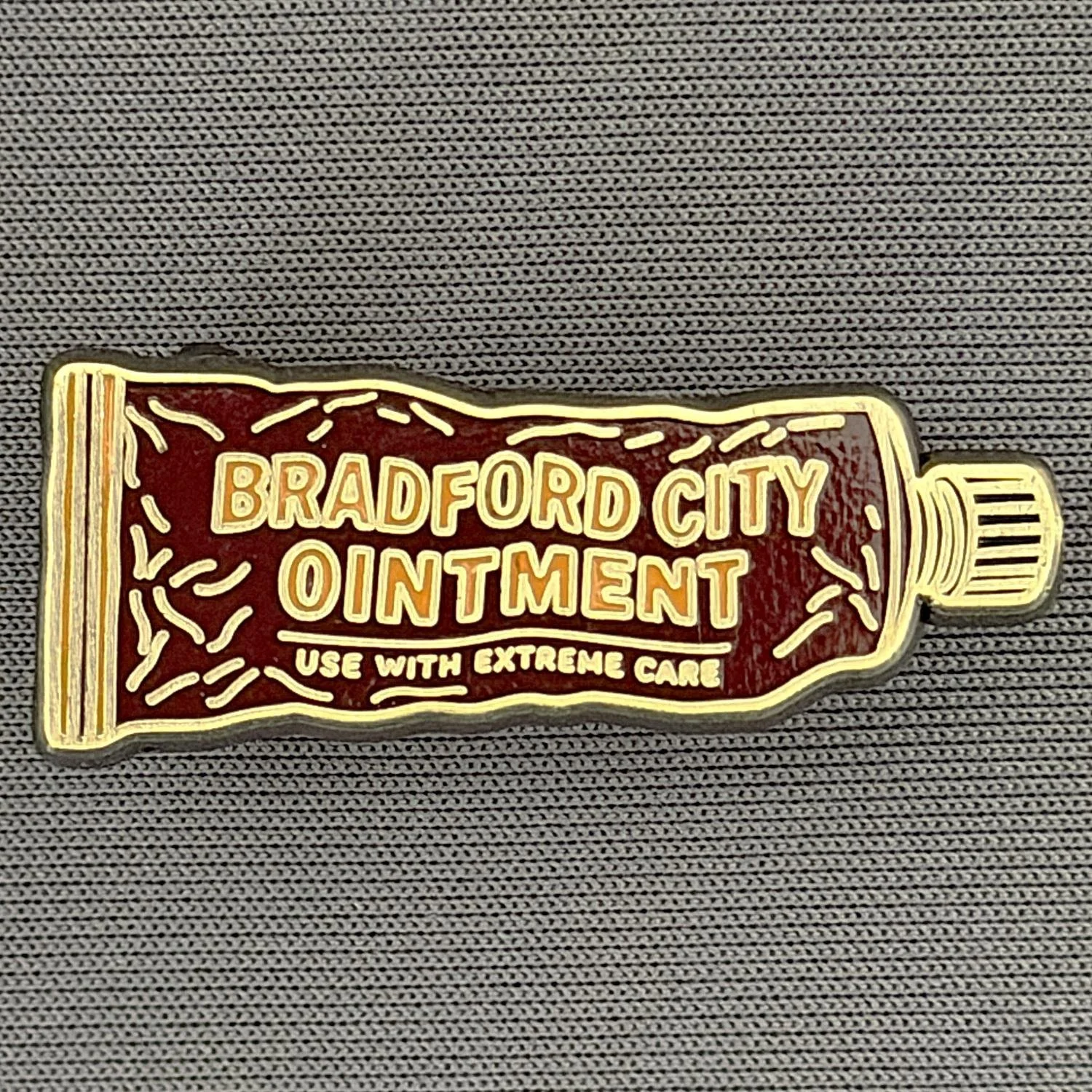 A patch shaped like a tube of ointment with the text "Bradford City Ointment" and "Use with Extreme Care" on it, placed on a textured gray surface.