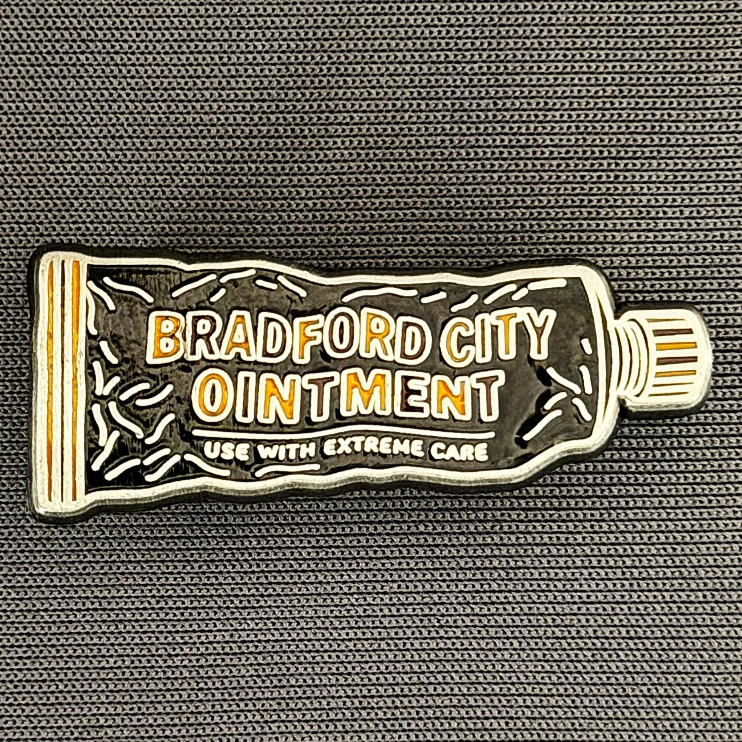A tube-shaped container with the text 'Bradford City Ointment' and 'Use with Extreme Care' printed on it, placed on a textured black surface.