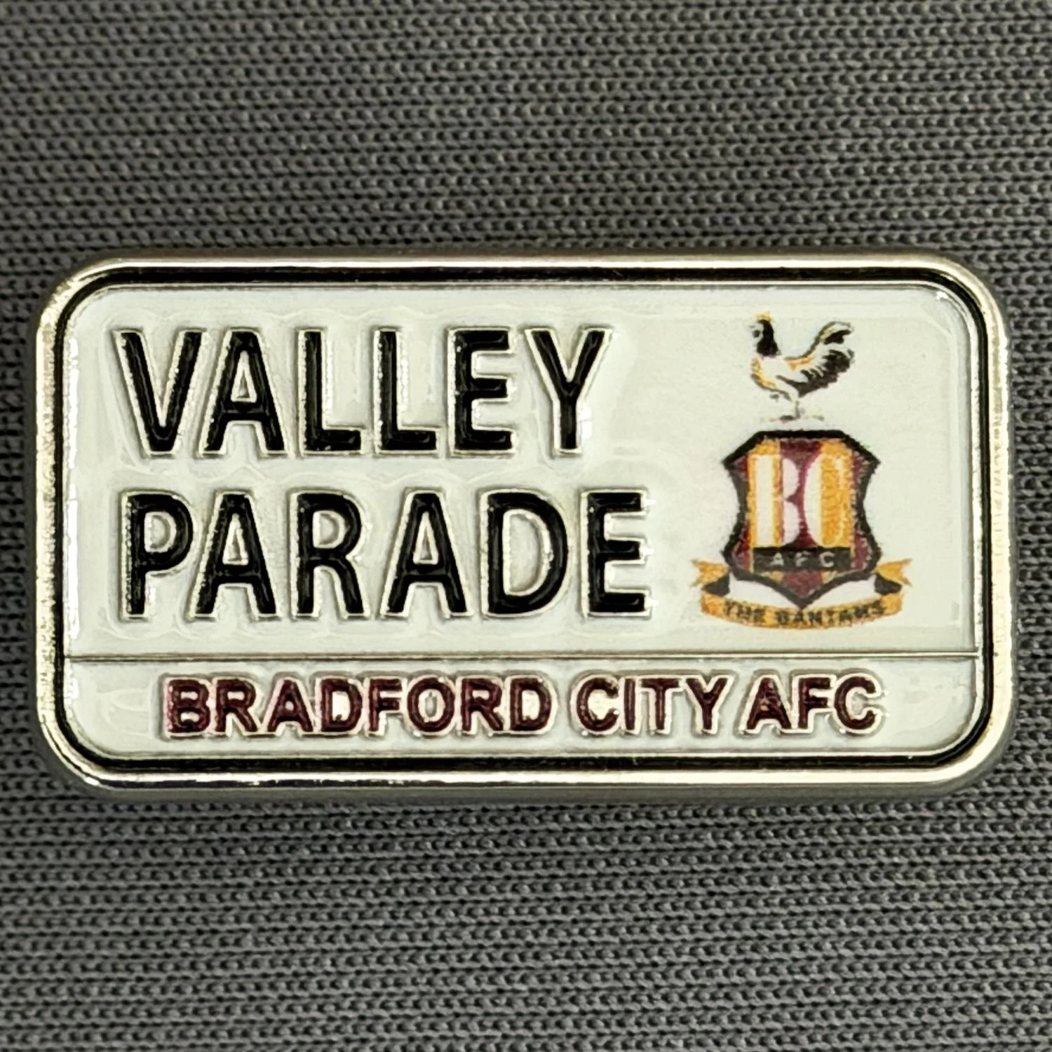 Reference Number: BCVP027
Size: H 14.2 mm x W 25.2 mm
Pin Type: Metal Clutch
Plating: Silver
Value: £4
Manufacturer: Bradford City Shop
Comments: Valley Parade Road Sign Printed Logo 2026