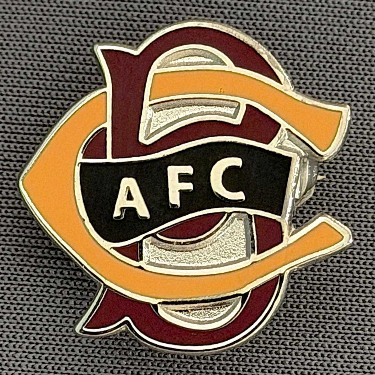 Reference Number: BCC&L072
Size: H 20.6 mm x 20.8  mm
Pin Type: Brooch Pin
Plating: Silver
Value: £6
Manufacturer: Unknown
Comments: BCFC Ayrton Scroll Claret & Amber, Black Centre Smaller Version