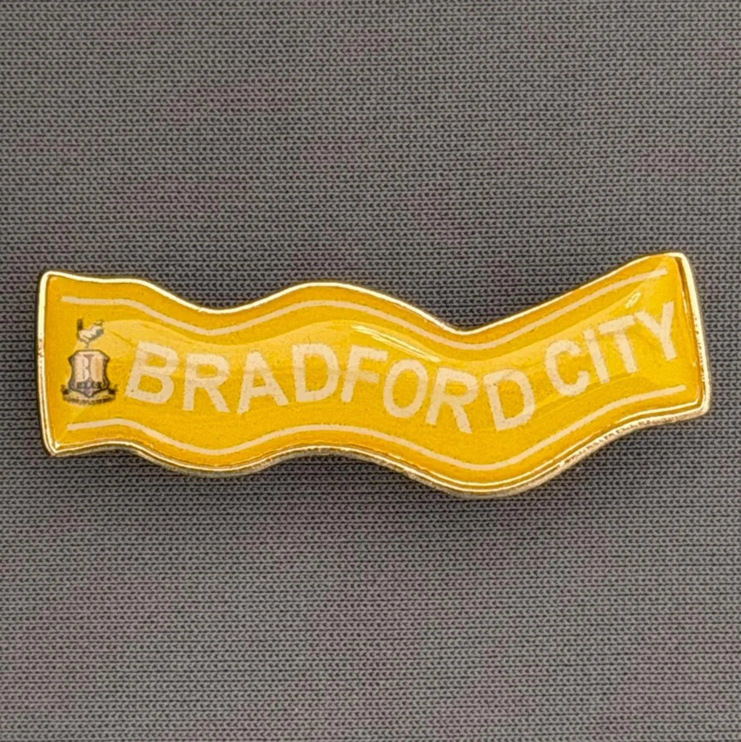 Reference Number: BCSCA010
Size: H 13.8 mm x W 39.7 mm
Pin Type: Brooch Pin
Plating: Gold
Value: £4
Manufacturer: Unknown
Comments: Yellow Bradford City Scarf with City Logo