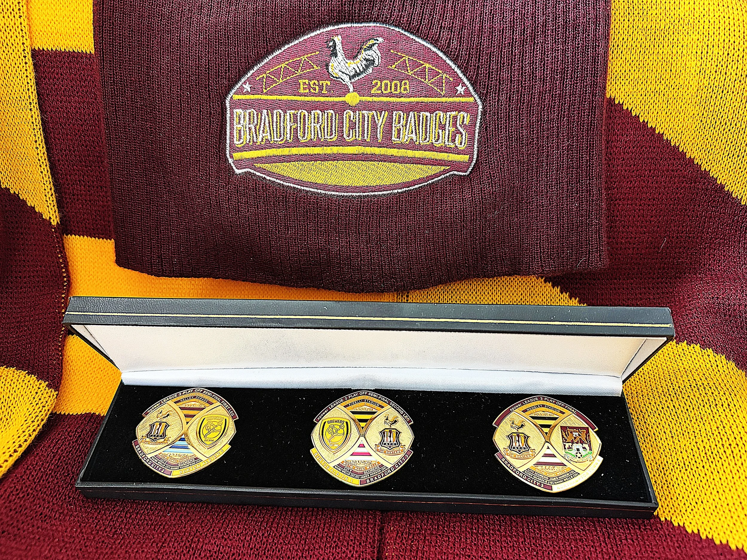Close-up of a fabric patch featuring a rooster and the text 'Bradford City Badges, Established 2004.' The patch is on a maroon background with yellow accents, likely part of a sports or fan apparel.