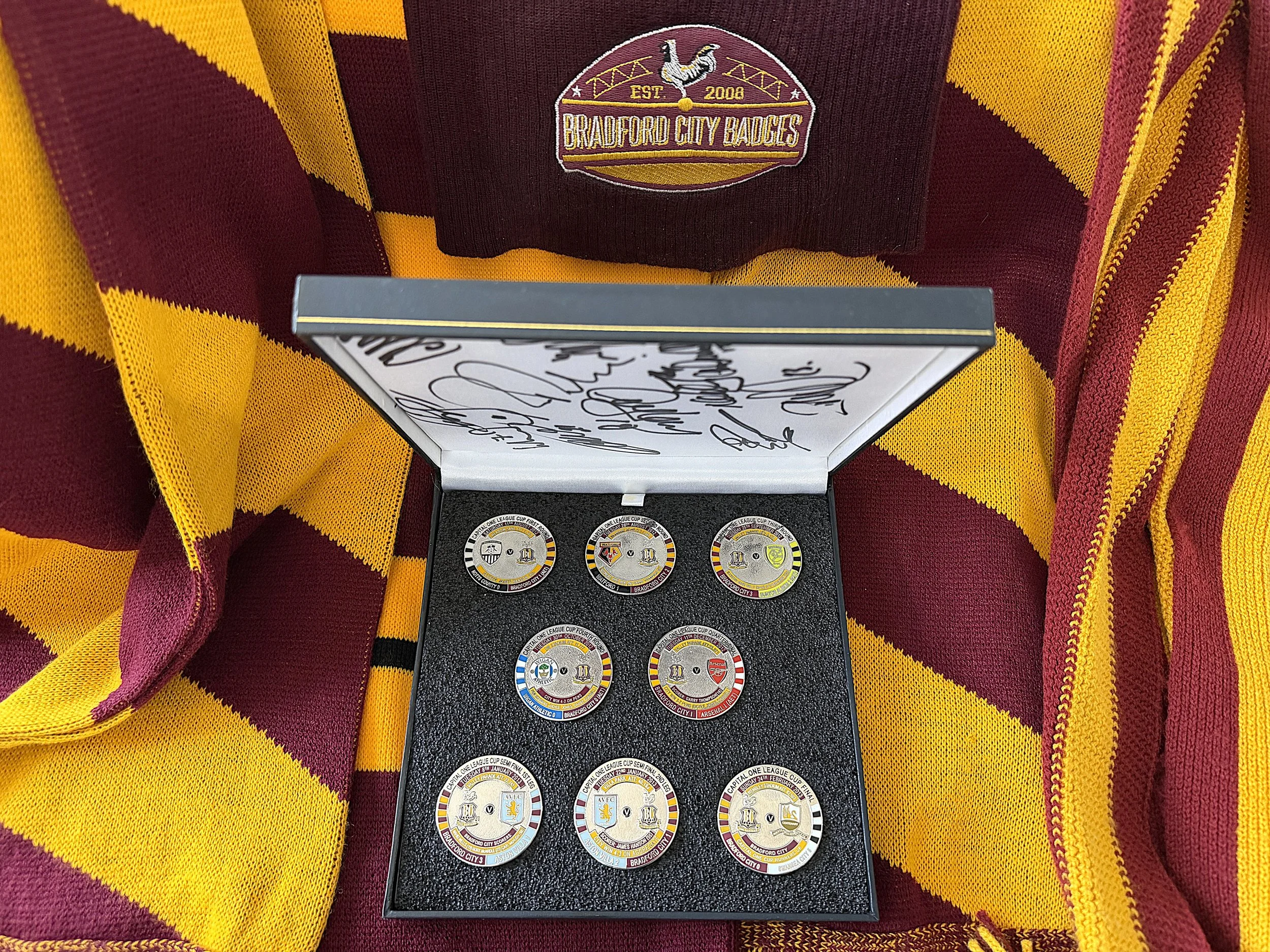 A collection of football or soccer league badges with various team logos displayed on a black holder, resting on a red and yellow striped fabric.