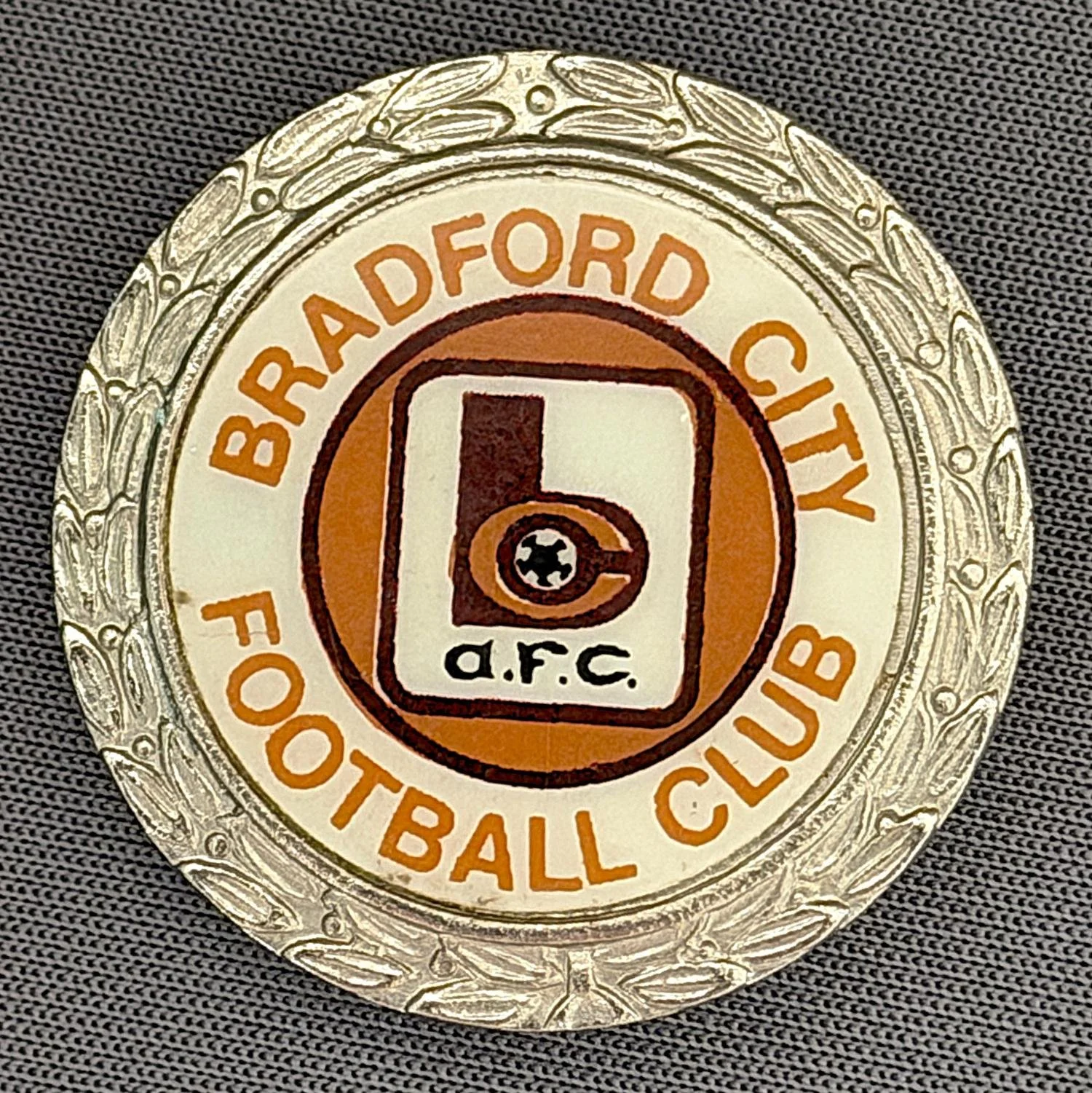 Reference Number: BCC&L007
Size: D 29.9 mm
Pin Type: Brooch Pin
Plating: Silver
Value: £12
Manufacturer: Clubman
Comments: Mid 70s Circular Laurel BC Plastic Insert