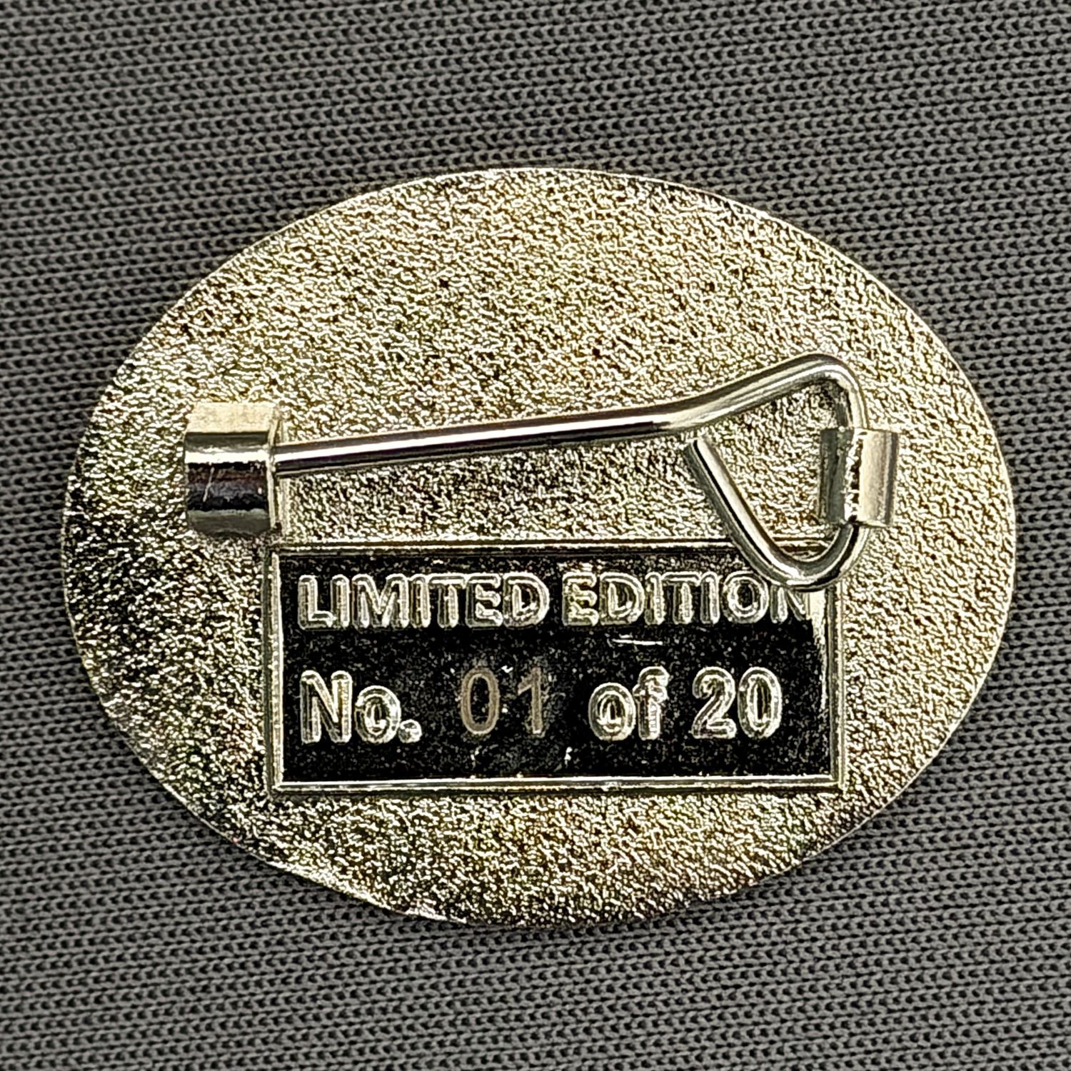 A metallic clothing label pin with a safety pin on the back, engraved with the words 'LIMITED EDITION' and a serial number 'No. 01 of 20', placed on dark fabric.