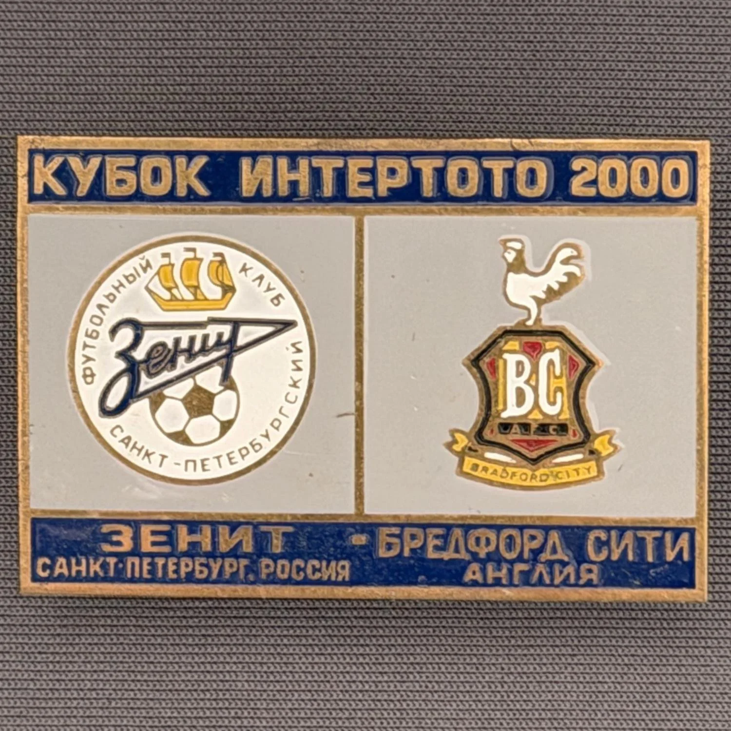 Reference Number: BCRUS020
Size: H 29.6 mm x W 44.6 mm
Pin Type: Metal Clutch
Plating: Antique Gold
Value: £12
Manufacturer: Unknown
Comments: Zenit St. Petersburg Inter Toto Cup, Dark Blue Top, Grey Middle, Dark Blue Bottom