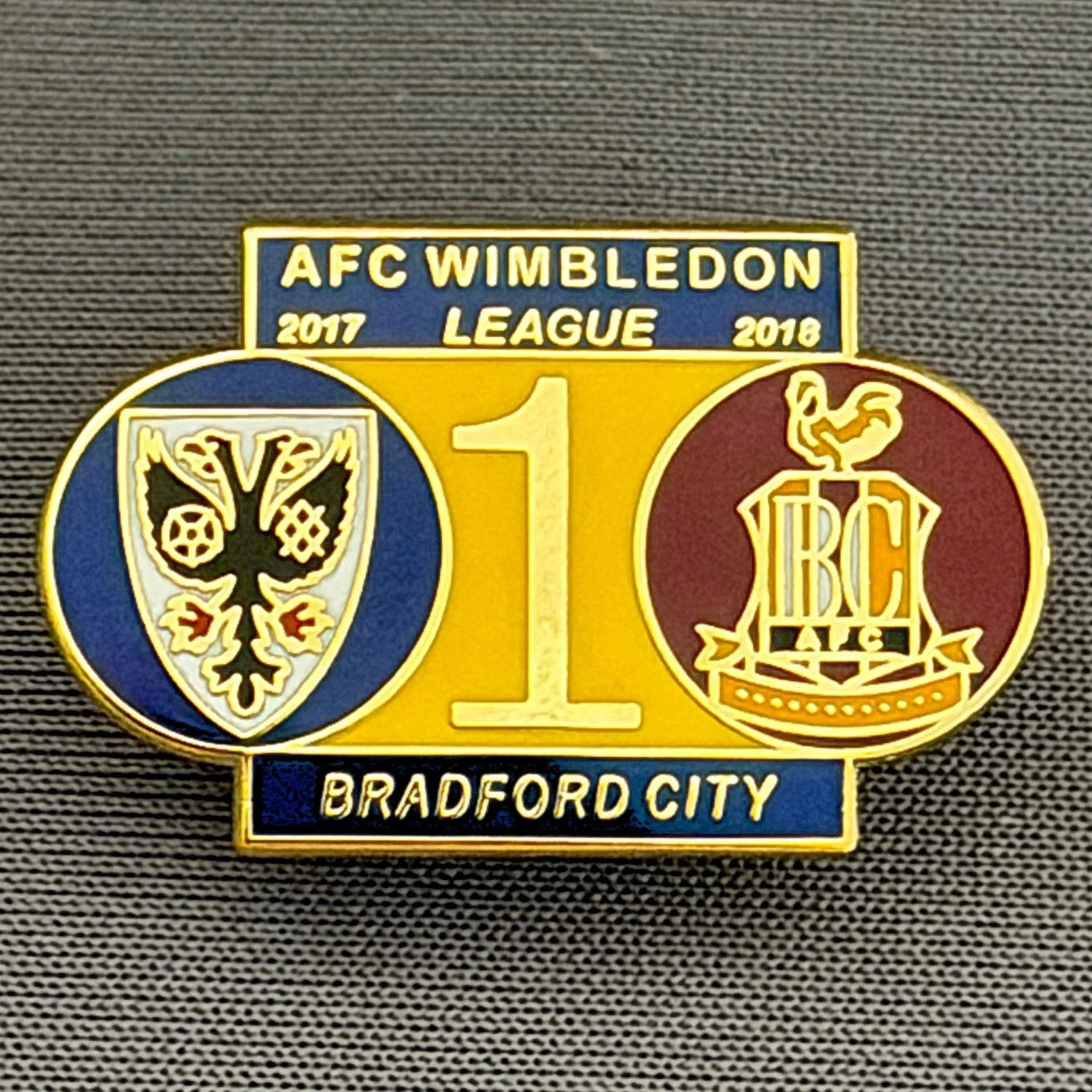 Reference Number: BCOFIX113
Size: H 16 mm x W 25.3 mm
Pin Type: Rubber Clutch
Plating: Gold
Value: £5
Manufacturer: Terry's Badges
Comments: A.F.C. Wimbledon v Bradford City, League One 2017/18 