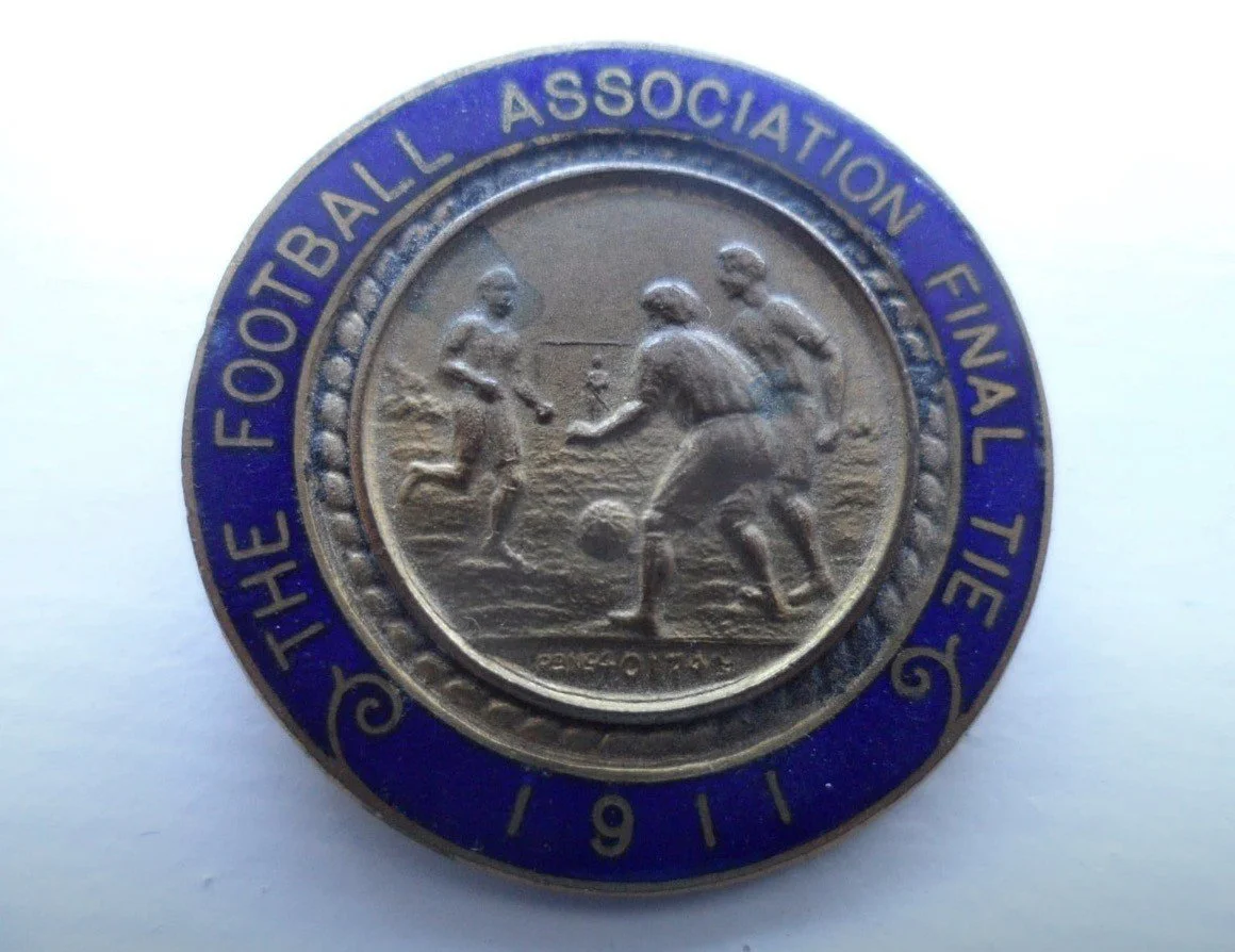 A coin commemorating the 1961 Football Association Final with an outer blue rim and gold inner circle featuring four players on a football field.