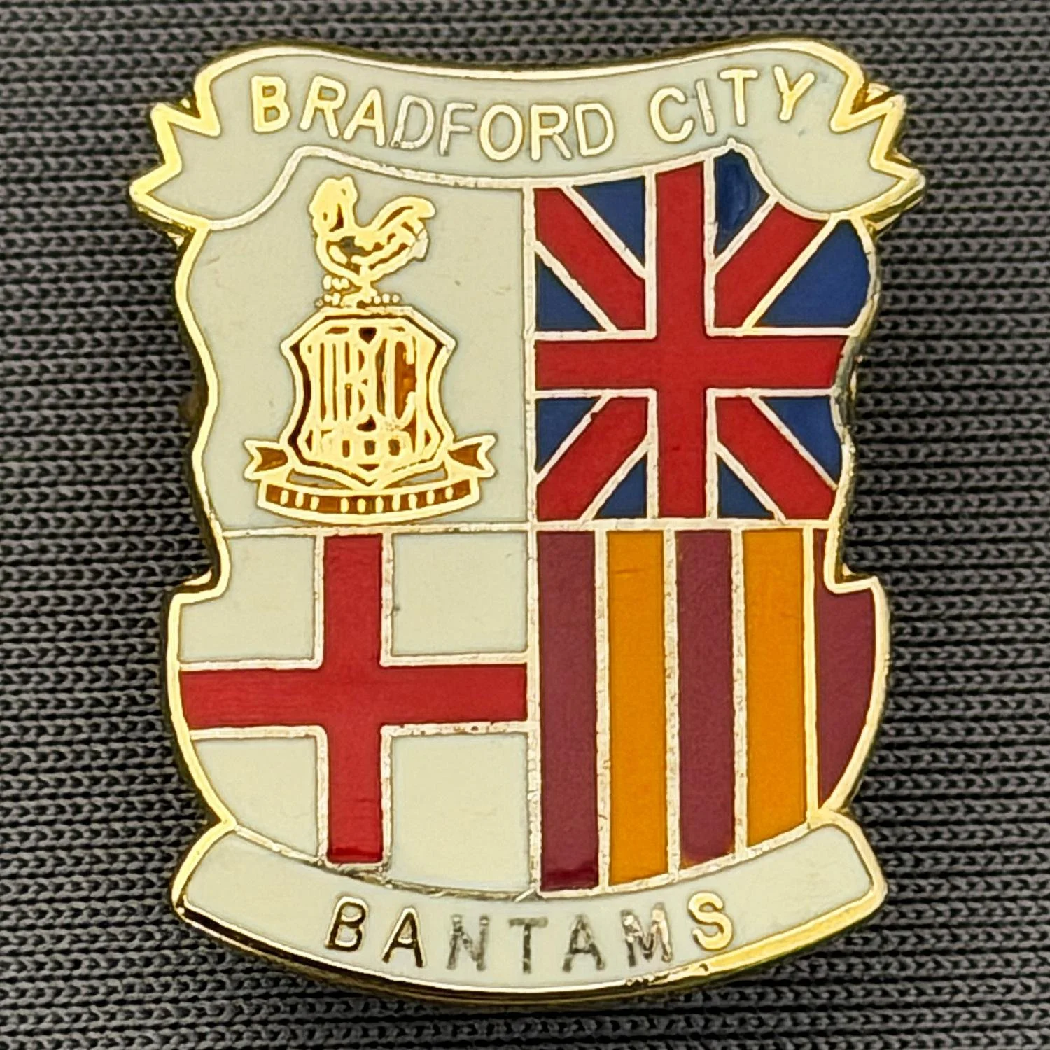 Reference Number: BCMUL013
Size: H 21.6 mm x W 17.7 mm
Pin Type: Brooch Pin
Plating: Gold
Value: £6
Manufacturer: Unknown
Comments: City Logo, Union Flag, St. George's Cross, Bantams, White Version