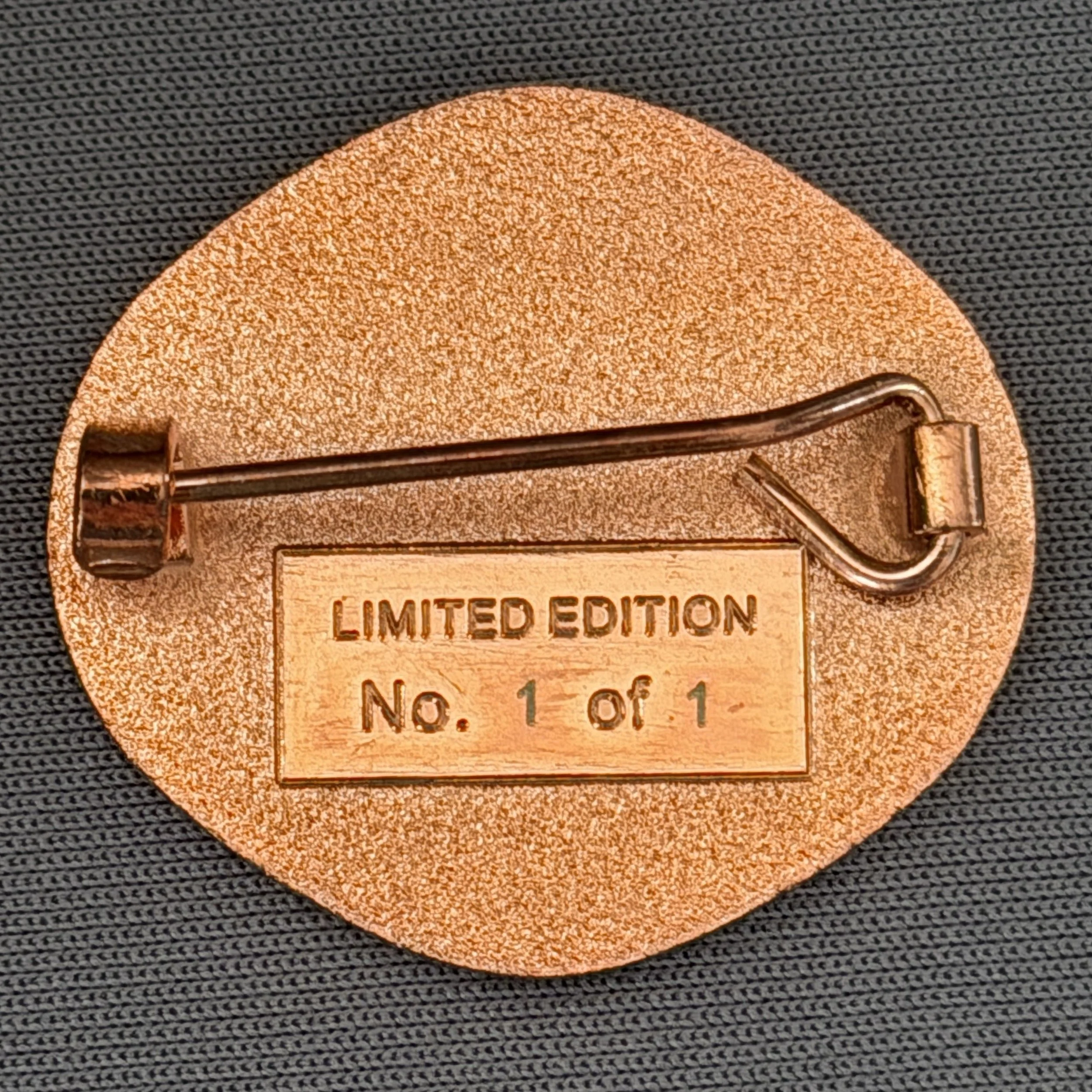 Close-up of a limited edition, circular light brown plaque with the words "LIMITED EDITION" engraved, featuring a metallic clasp on the side, against a dark, textured fabric background.