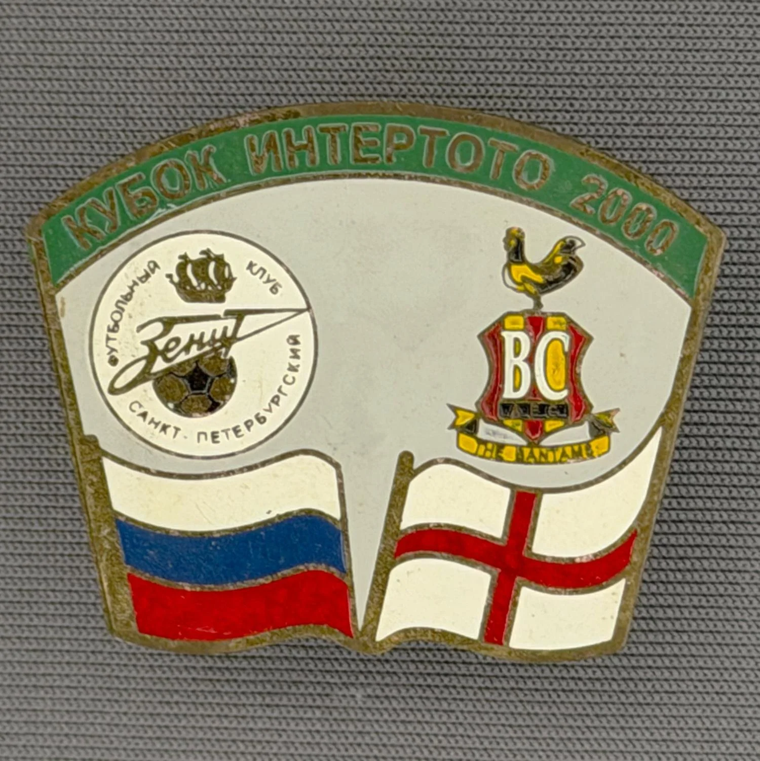 Reference Number: BCRUS046
Size: H 26 mm x W 32.3 mm
Pin Type: Metal Clutch
Plating: Antique Gold
Value: £12
Manufacturer: Unknown
Comments: Zenit St. Petersburg Inter Toto Cup, Green Top, Grey Background, Yellow Bantam