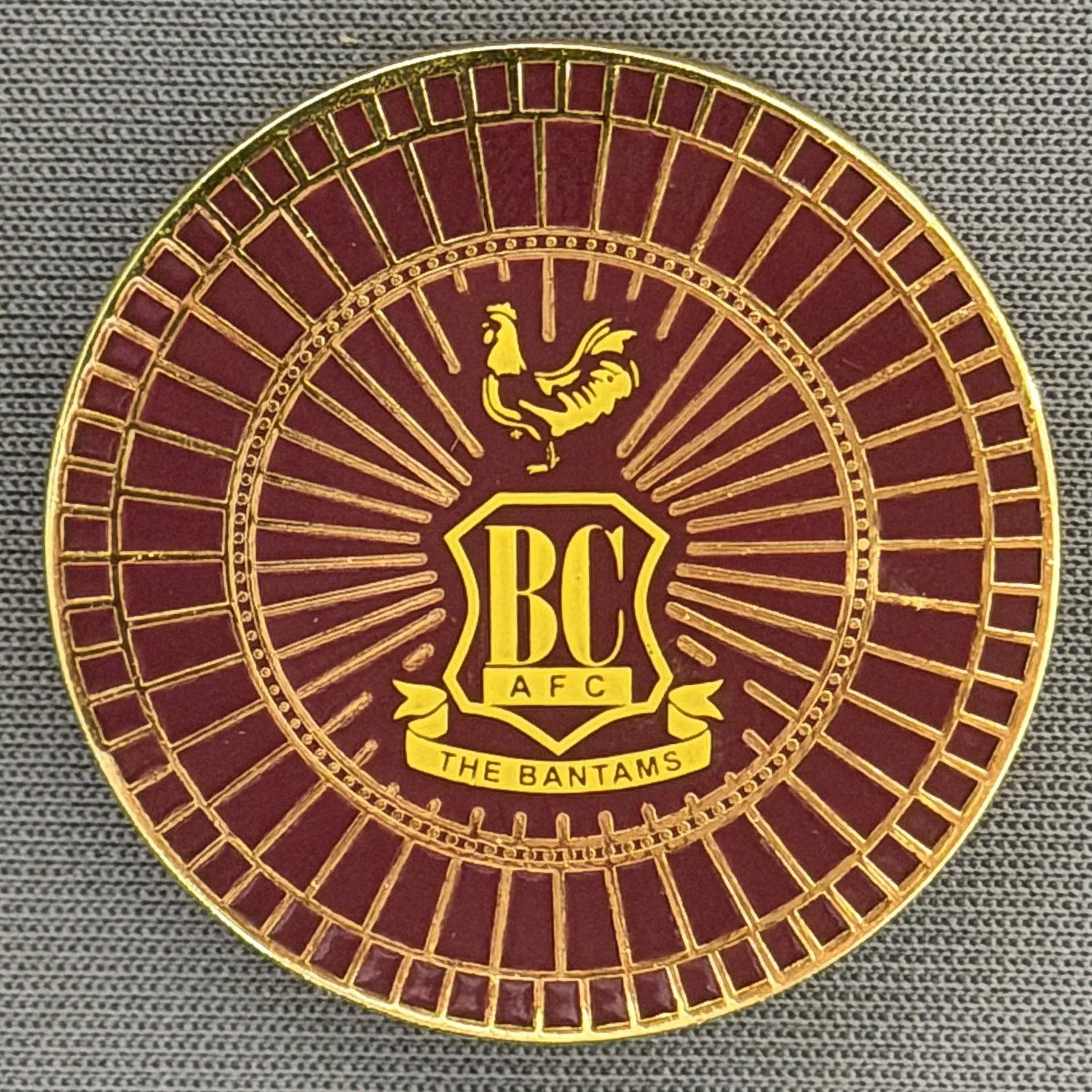Reference Number: BCC&L168
Size: D 30.4 mm
Pin Type: Metal Clutch
Plating: Gold
Value: £6
Manufacturer: Bradford City Shop
Comments: Circular Spoke Wheel Claret City Crest
