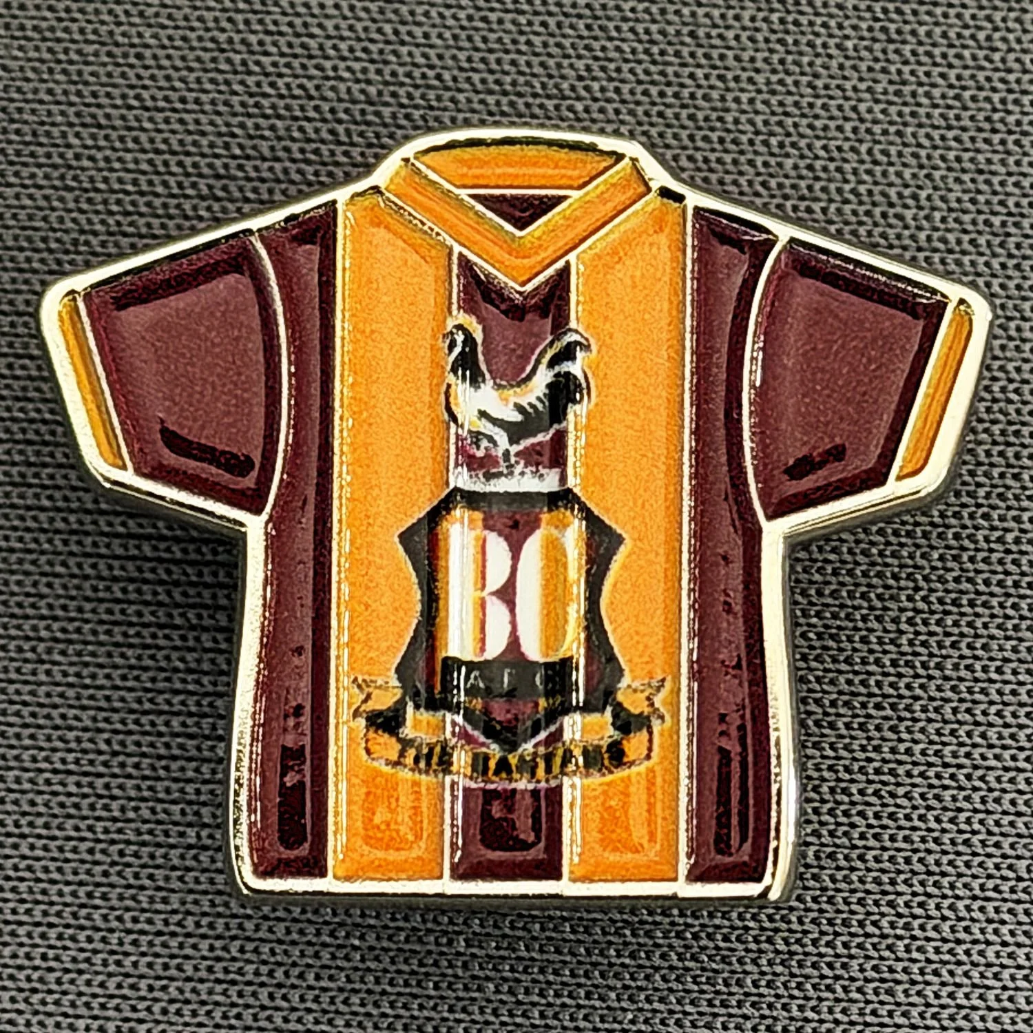 A pin badge featuring a stylized human torso with a skull on the chest, wearing a shirt with vertical stripes in yellow, orange, and red, and a large 