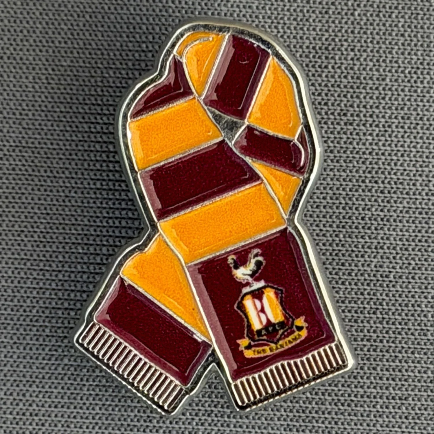 Reference Number: BCSCA013
Size: H 24.9 mm x W 18 mm
Pin Type: Metal Clutch
Plating: Silver
Value: £4
Manufacturer: Bradford City Shop
Comments: Claret & Amber Scarf with Printed City Logo 2026