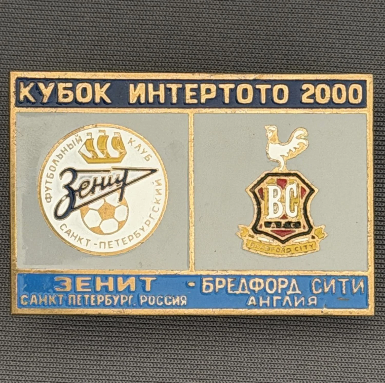 Reference Number: BCRUS021
Size: H 29.6 mm x W 44.6 mm
Pin Type: Metal Clutch
Plating: Antique Gold
Value: £12
Manufacturer: Unknown
Comments: Zenit St. Petersburg Inter Toto Cup, Dark Blue Top, Grey Middle, Mid Blue Bottom