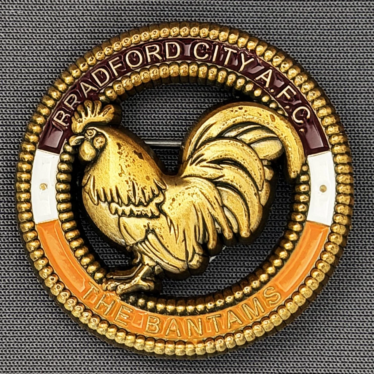 Reference Number: BCBAN073
Size: D 35.3 mm
Pin Type: Brooch Pin
Plating: Antique Gold
Value: £12
Manufacturer: Bradford City Badges
Comments: 3D Claret, Amber & White, Cut Out Bantam. Limited Edition of 6 Badges.