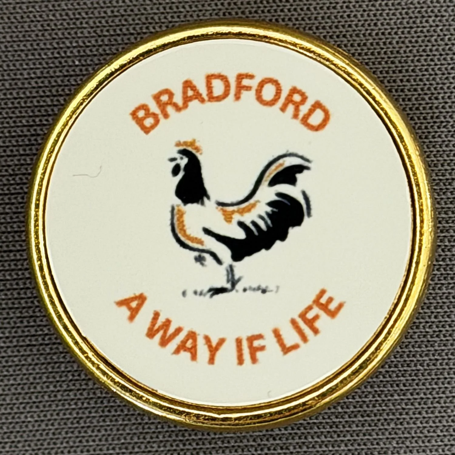 A round button with a gold border and an illustration of a rooster. The words 'Bradford' at the top and 'Always Life' at the bottom are written in orange text.
