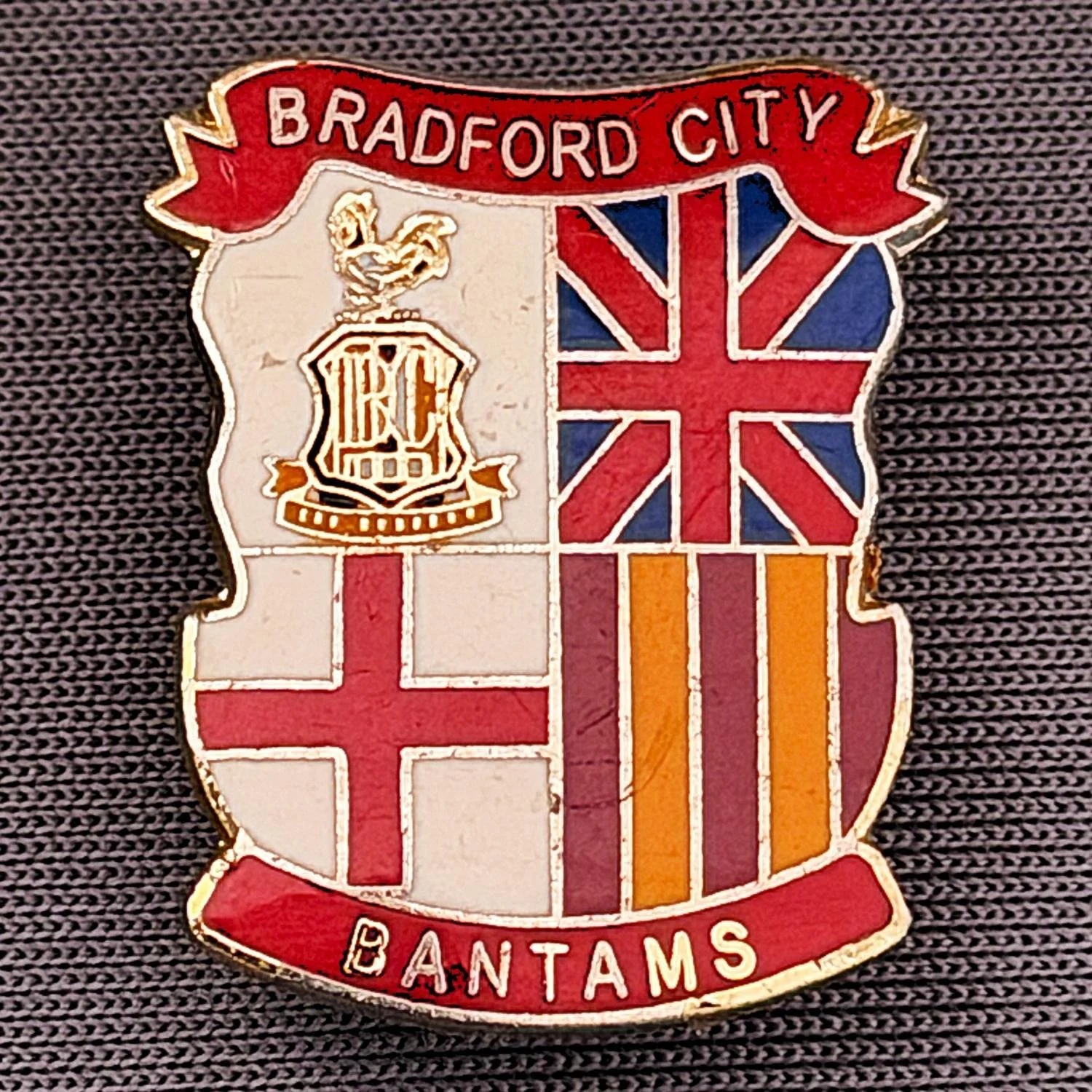 Reference Number: BCMUL012
Size: H 21.6 mm x W 17.7 mm
Pin Type: Brooch Pin
Plating: Gold
Value: £6
Manufacturer: Unknown
Comments: City Logo, Union Flag, St. George's Cross, Bantams, Red Version