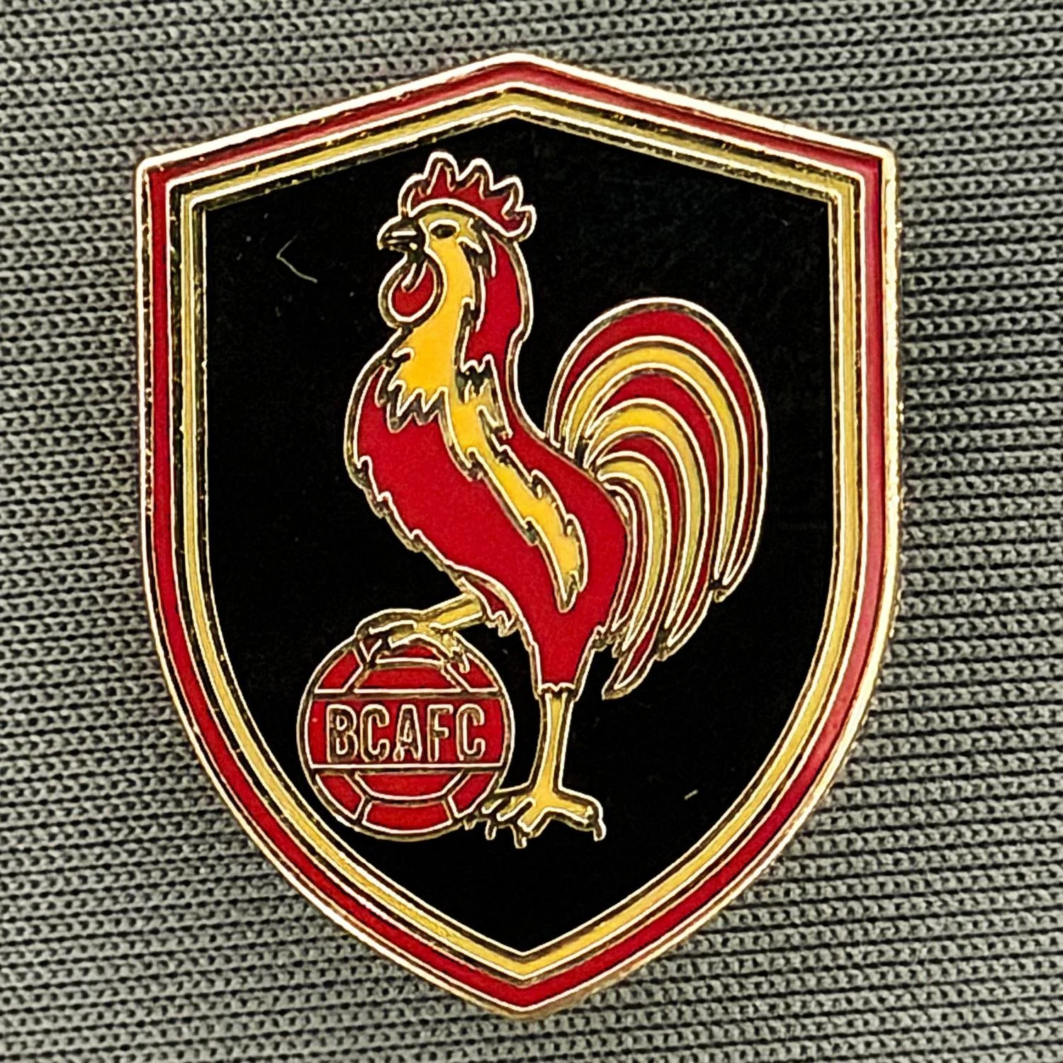 Reference Number: BCBAN084
Size: H 24.5 mm x W 19.3 mm
Pin Type: Brooch Pin
Plating: Gold
Value: £4
Manufacturer: Guy Badge Stall
Comments: Black Bantam Ball Shield 2026