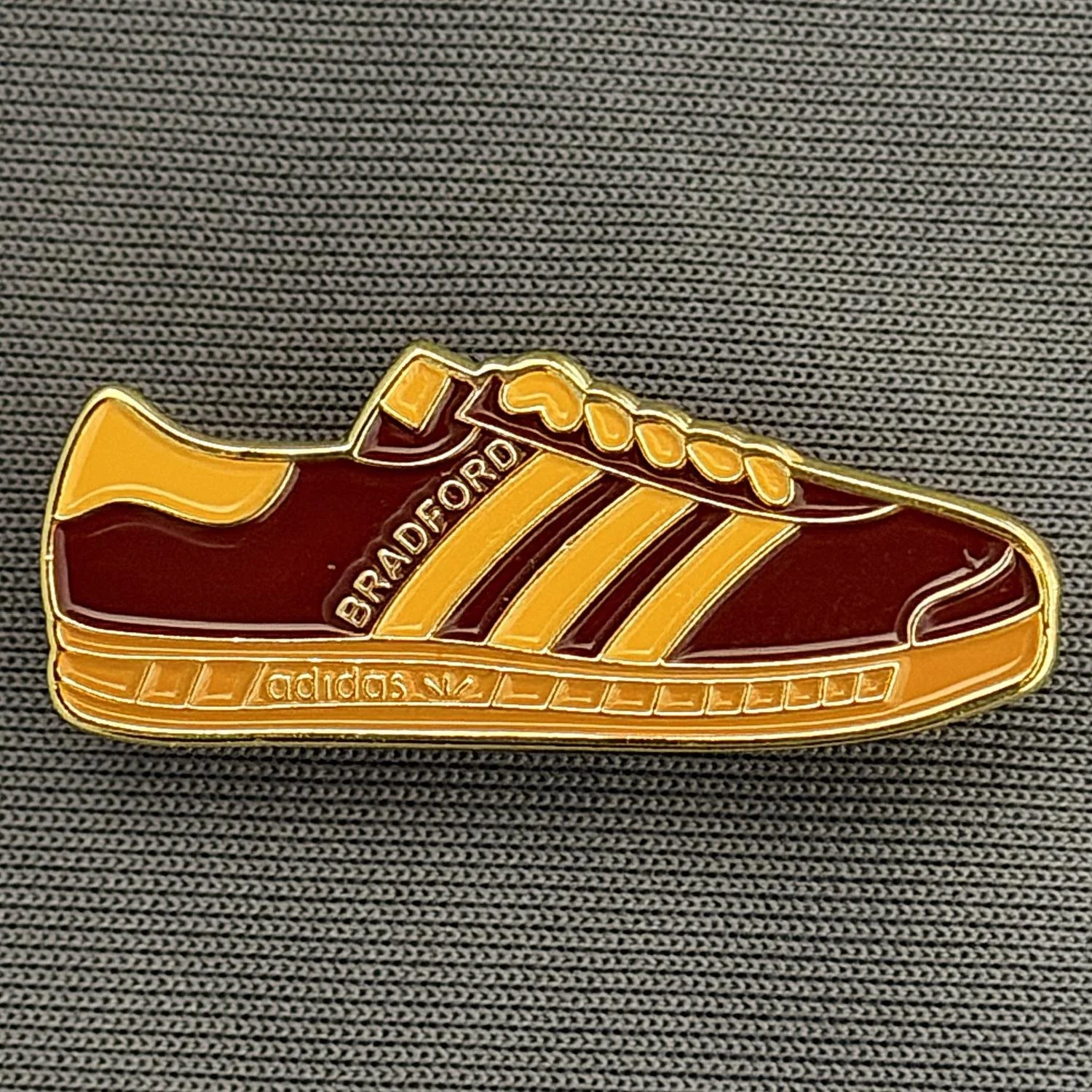Reference Number: BCUN043
Size: H 12.2 mm x W 30.4 mm
Pin Type: Brooch Pin
Plating: Gold
Value: £5
Manufacturer: Unknown
Comments: Claret & Amber Trainer, Large Version