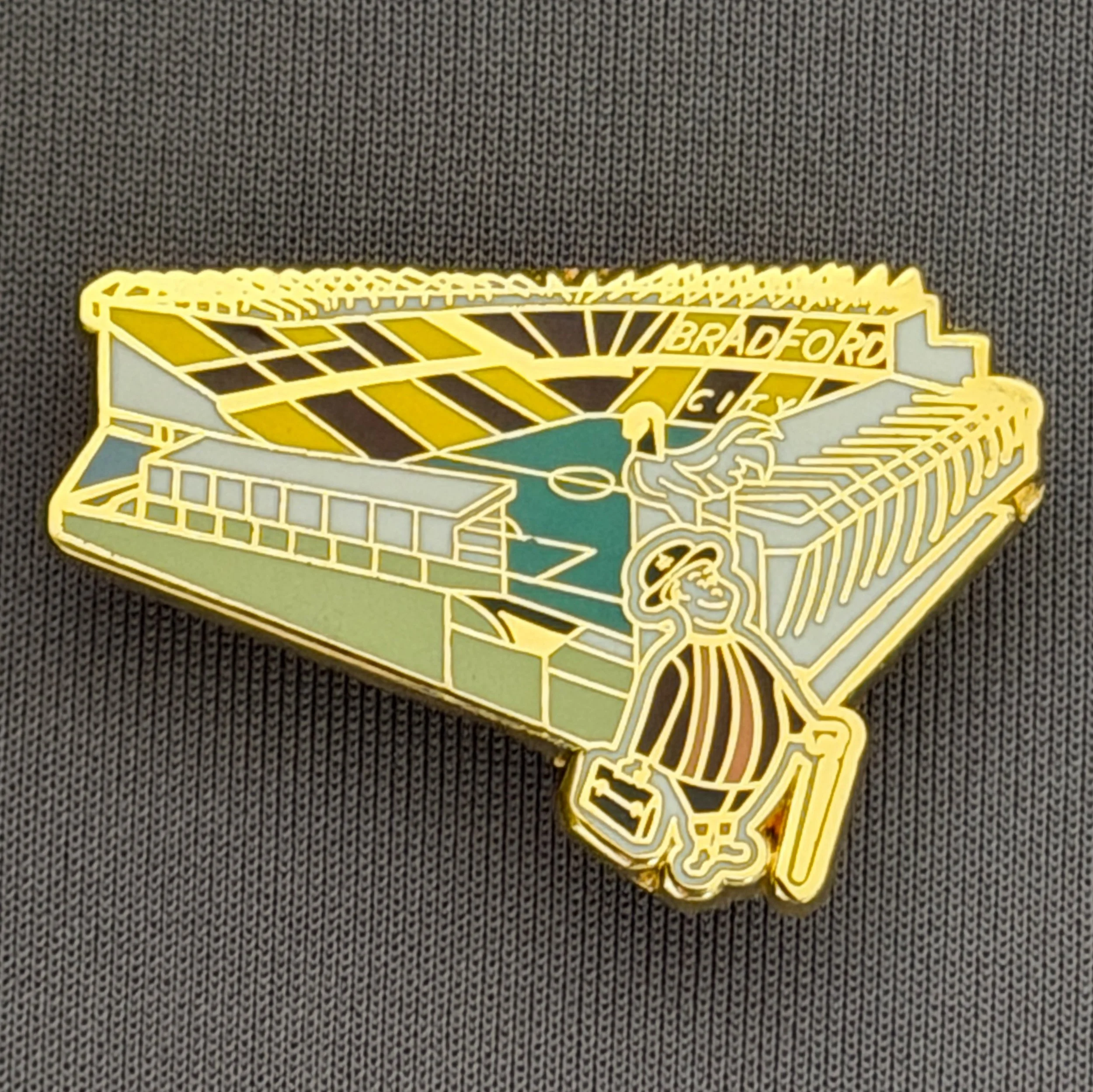 Reference Number: BCVP018
Size: H 22.3 mm x W 35.6 mm
Pin Type: Brooch Pin
Plating: Silver
Value: £6
Manufacturer: Unknown
Comments: Valley Parade Stadium with City Gent