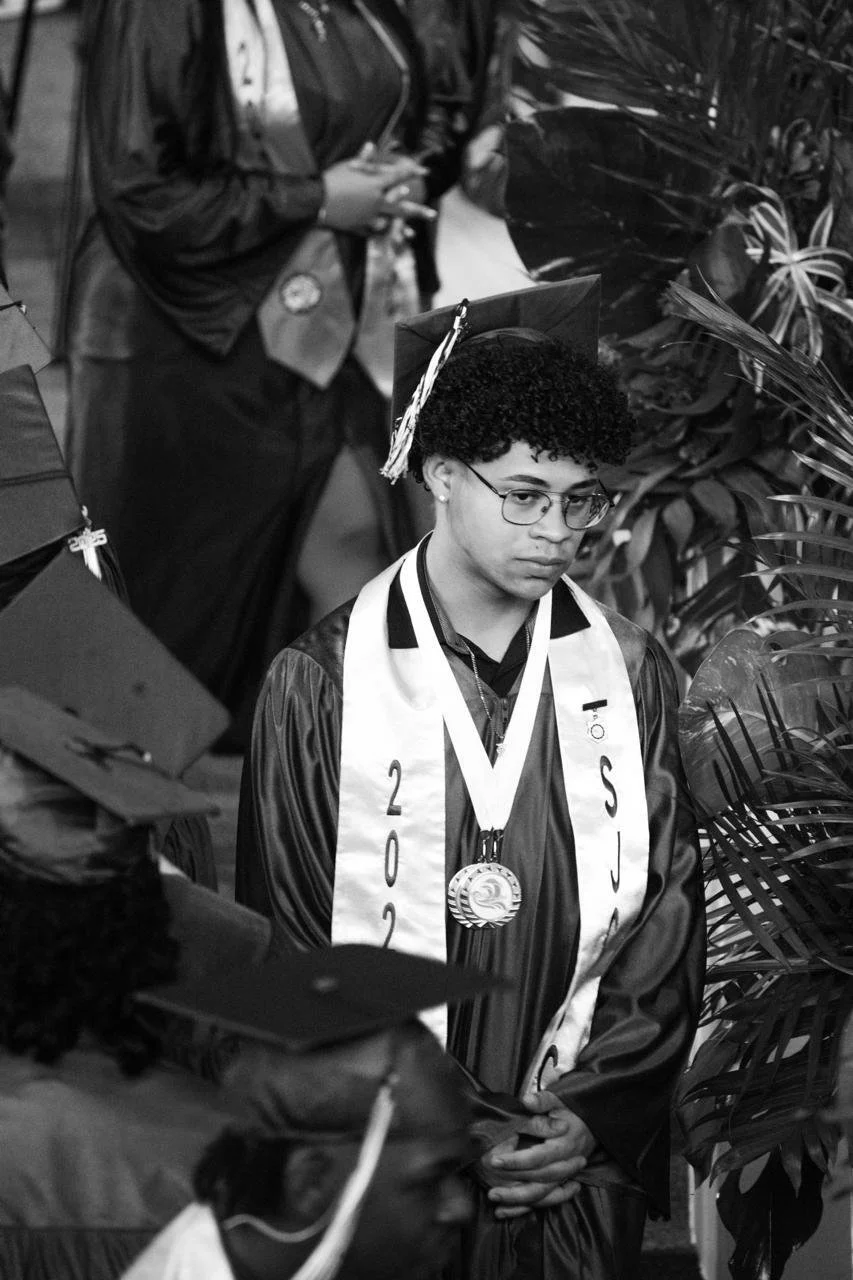 A young man in graduation cap and gown with a medal and sash, attending his graduation ceremony.
