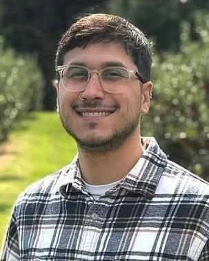 Photo of Antonio Cintron, a smiling young man wearing glasses and a white plaid shirt.