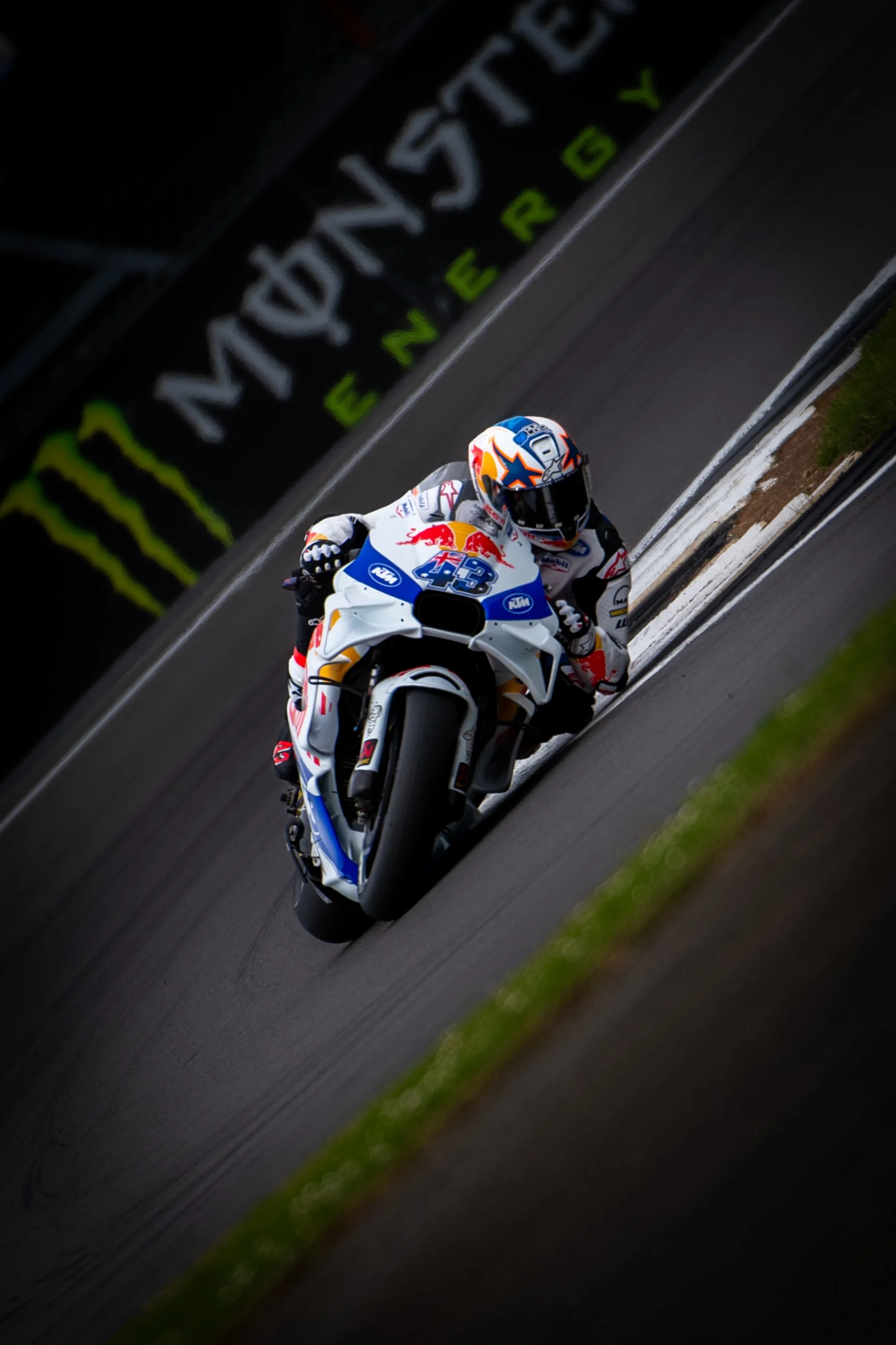 Motorcycle racer leaning into a turn on a race track, with a Monster Energy banner in the background.