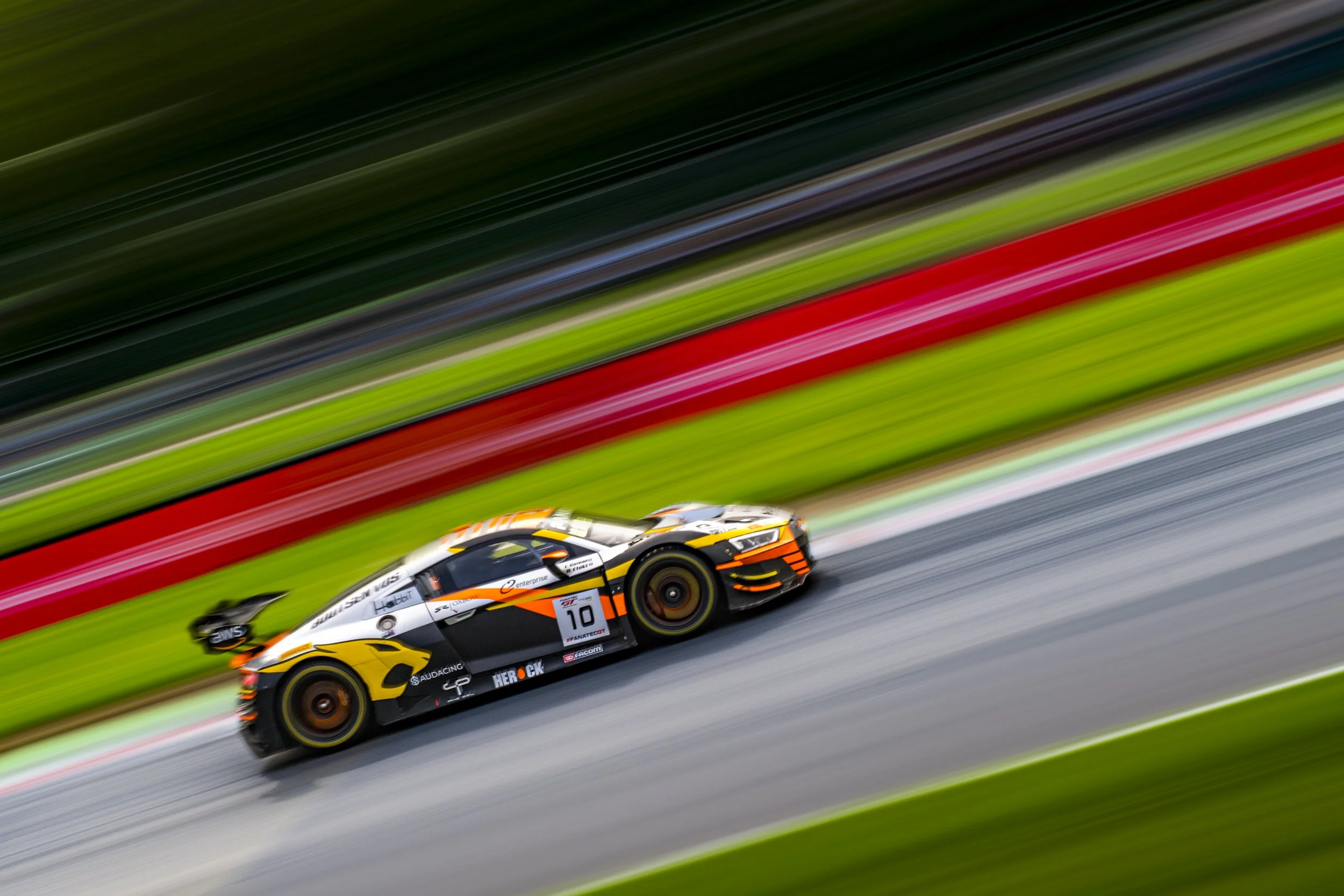 A race car speeding on a track with motion blur background and colorful barriers.