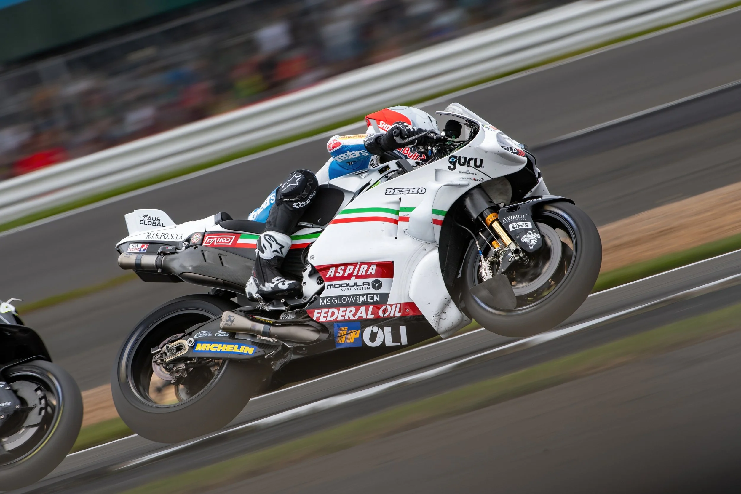 Motorcycle race car with a rider leaning into a turn on a racetrack, with blurred background and tire smoke.