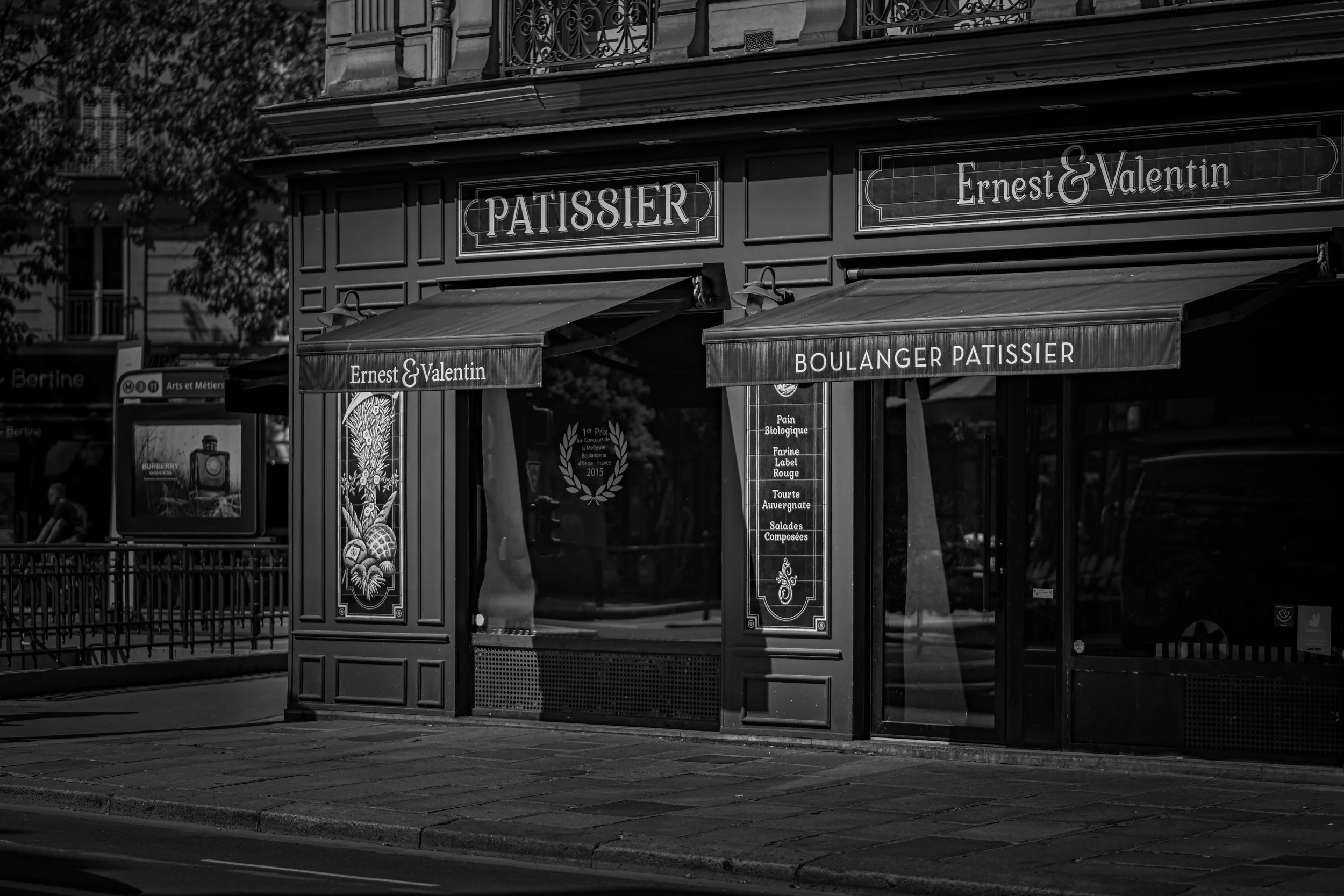 Black and white photo of a Parisian bakery storefront with signs reading 'Ernest & Valentin' and 'Boulanger Pâtissier', including decorative elements and menu written in French.