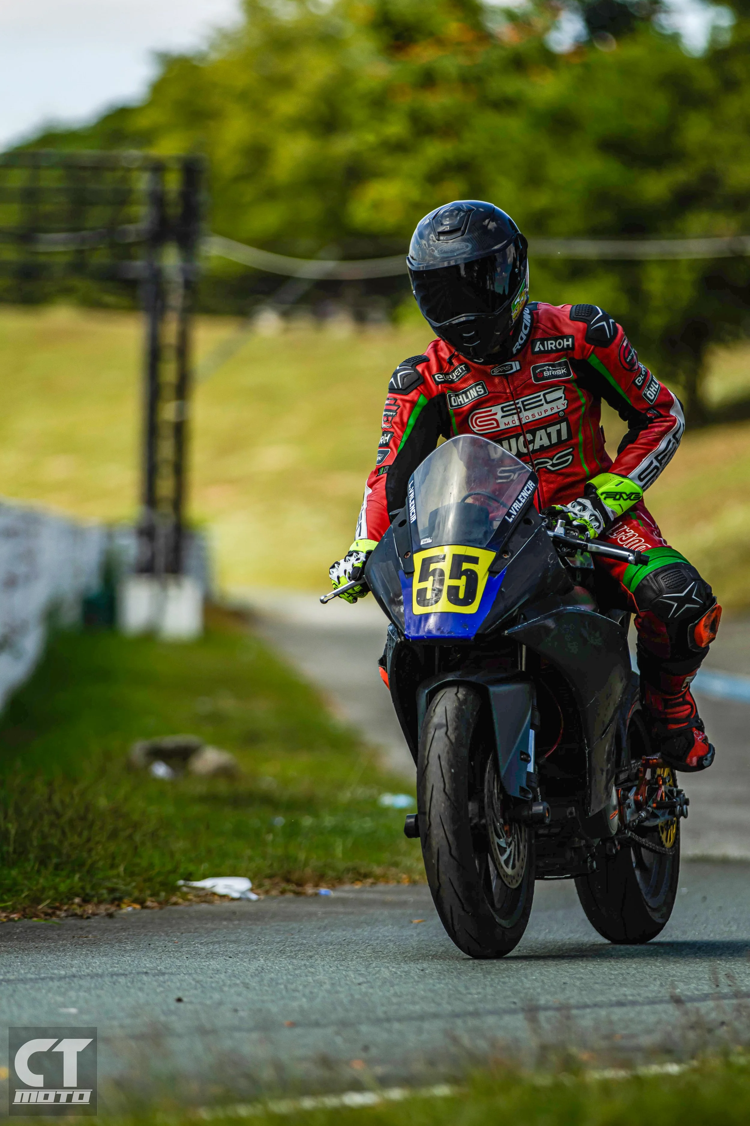 Lawrence Valencia racer wearing a black helmet and red racing suit riding a black motorcycle with the number 55 on the front on a racetrack.