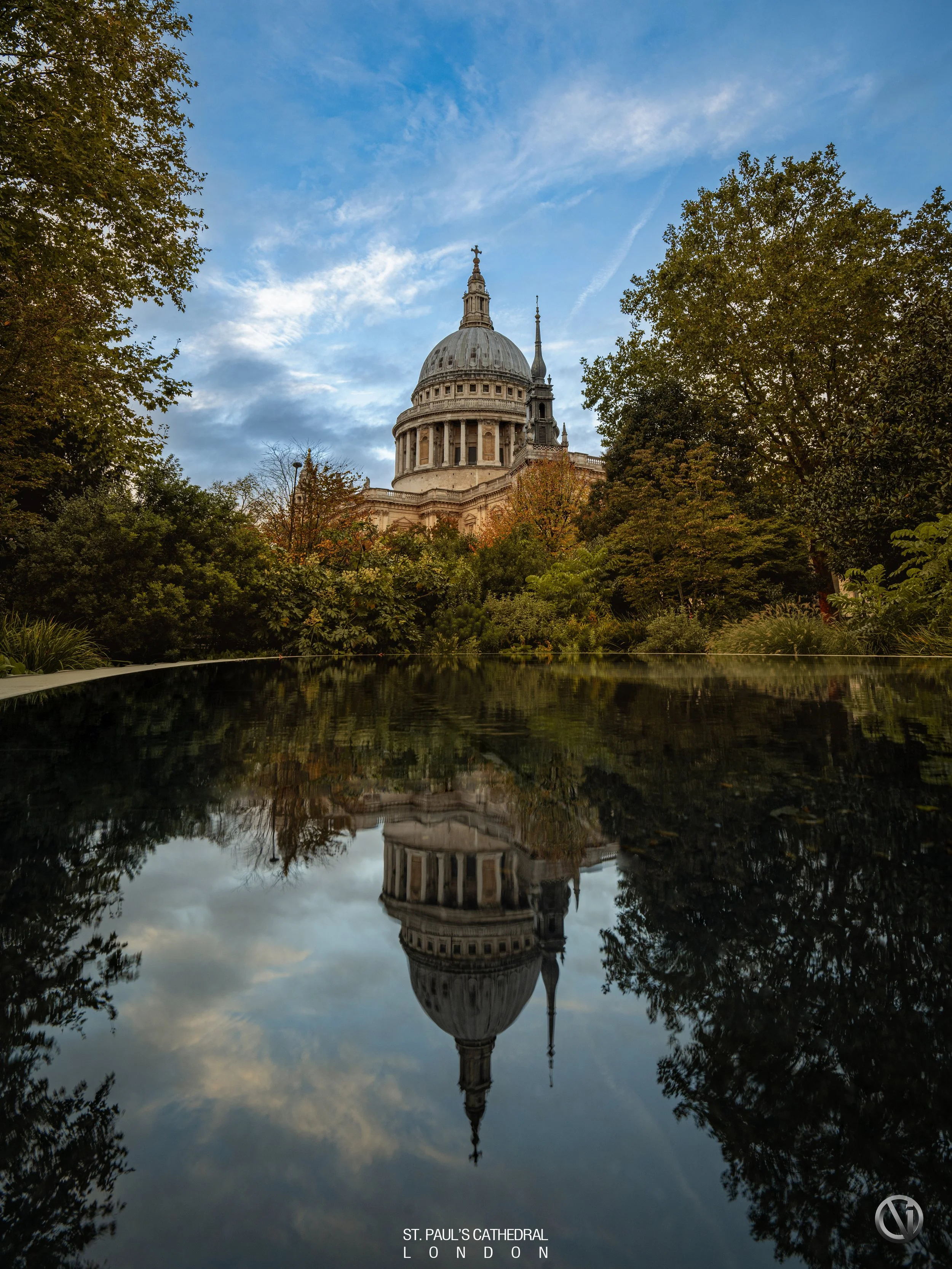 St. Paul's Cathedral in London seen through a pond's reflection with trees surrounding it, under a partly cloudy sky.