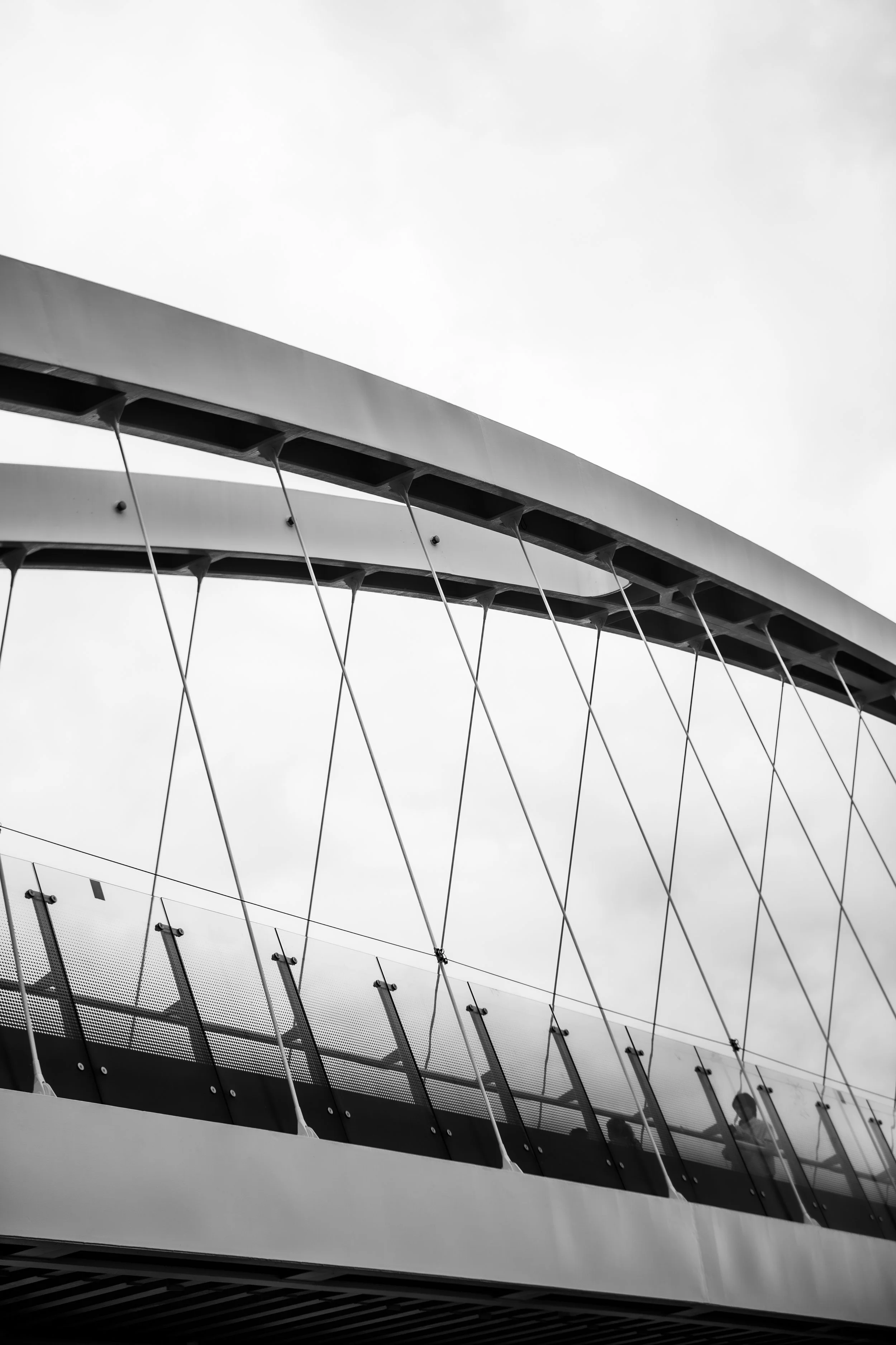 Black and white photo of a modern building's glass and metal structure, with a man walking along the enclosed balcony or walkway.