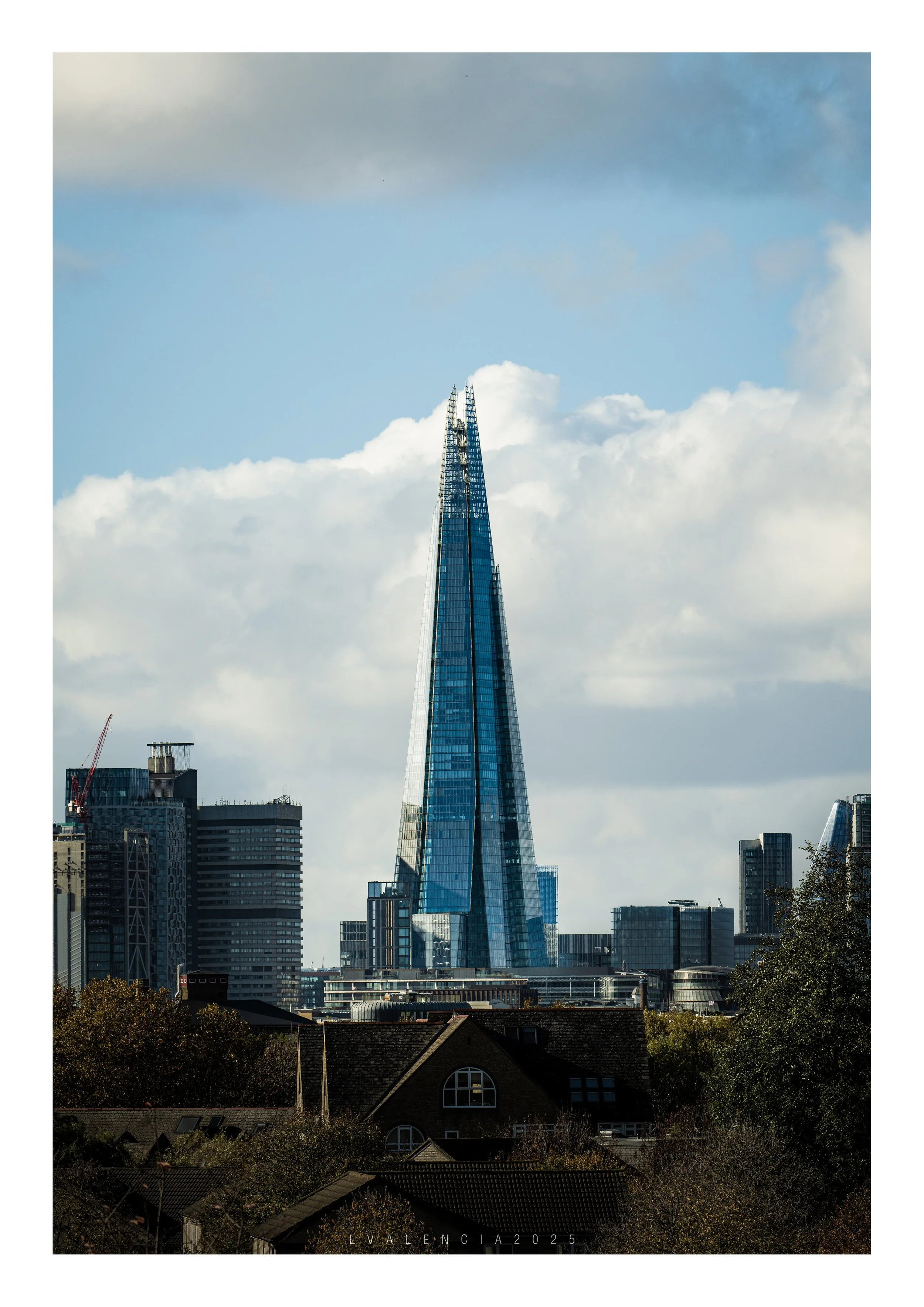 A cityscape featuring the modern skyscraper The Shard in London, England, with clouds in the sky and some buildings in the foreground.