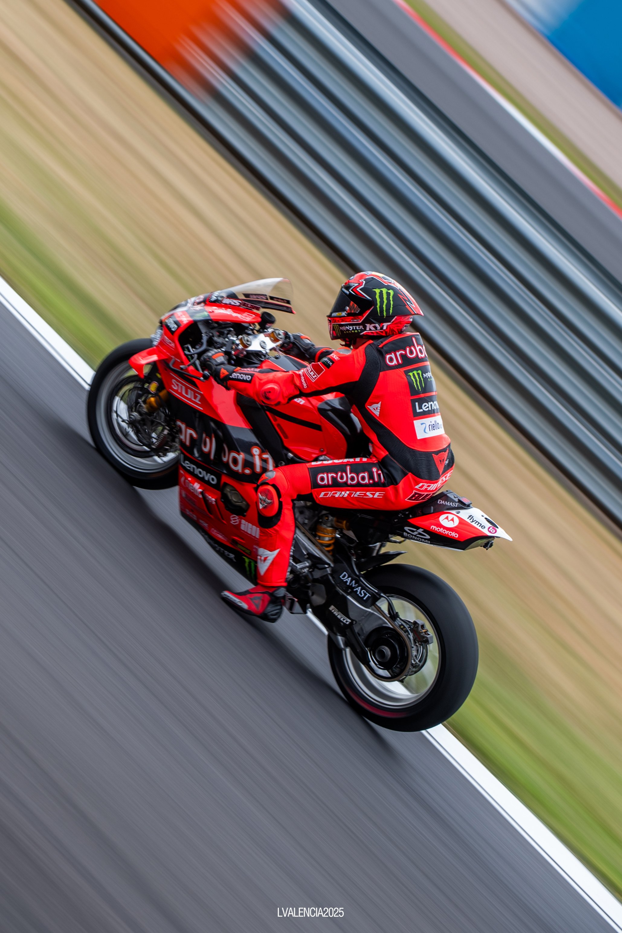 Motorcycle racer in red racing gear riding a red racing motorcycle on a racetrack with a blurred background.