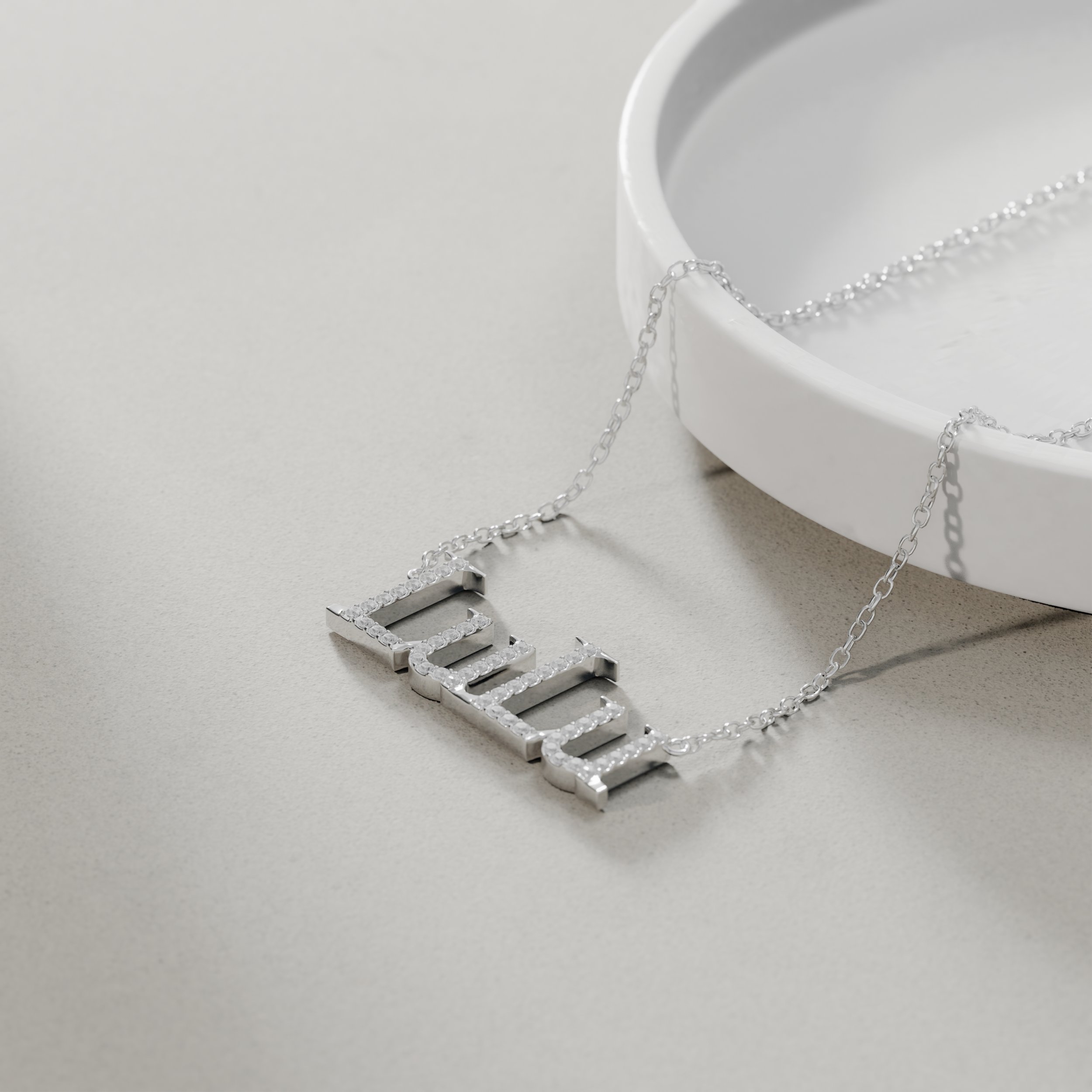 Silver necklace with the word "LIFE" encrusted with small stones, resting on a light-colored surface next to a white dish.