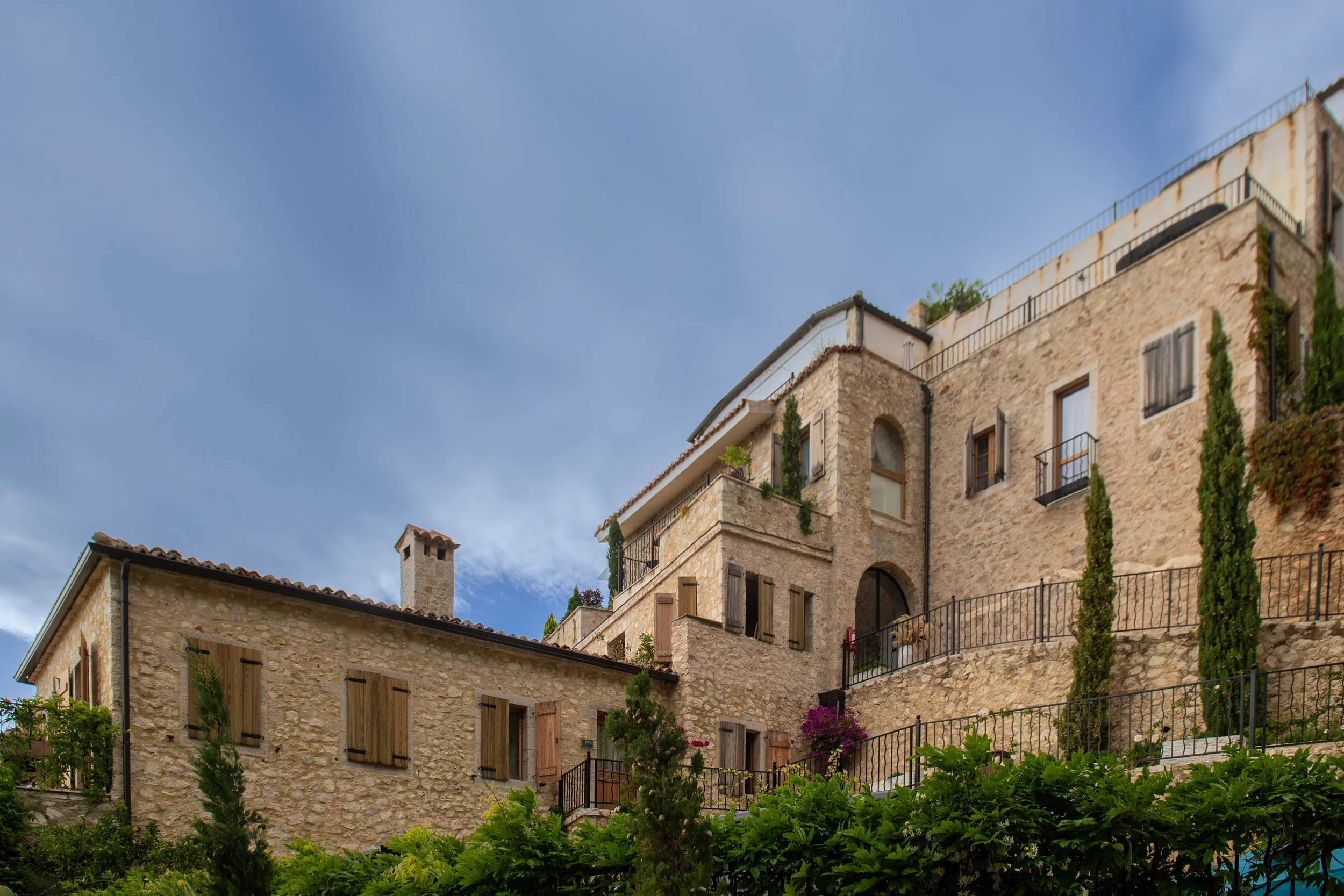 Stone houses with wooden shutters and balconies on a hillside under a blue sky.
