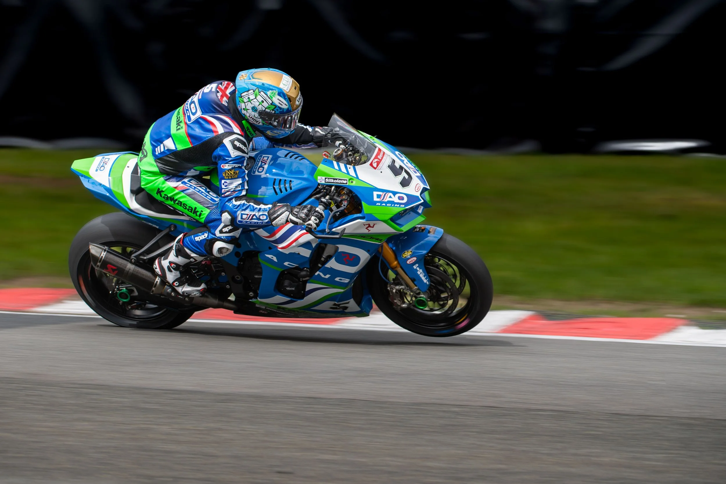 A motorcycle racer in racing gear leaning into a turn on a blue racing bike with Kawasaki branding, on a race track.
