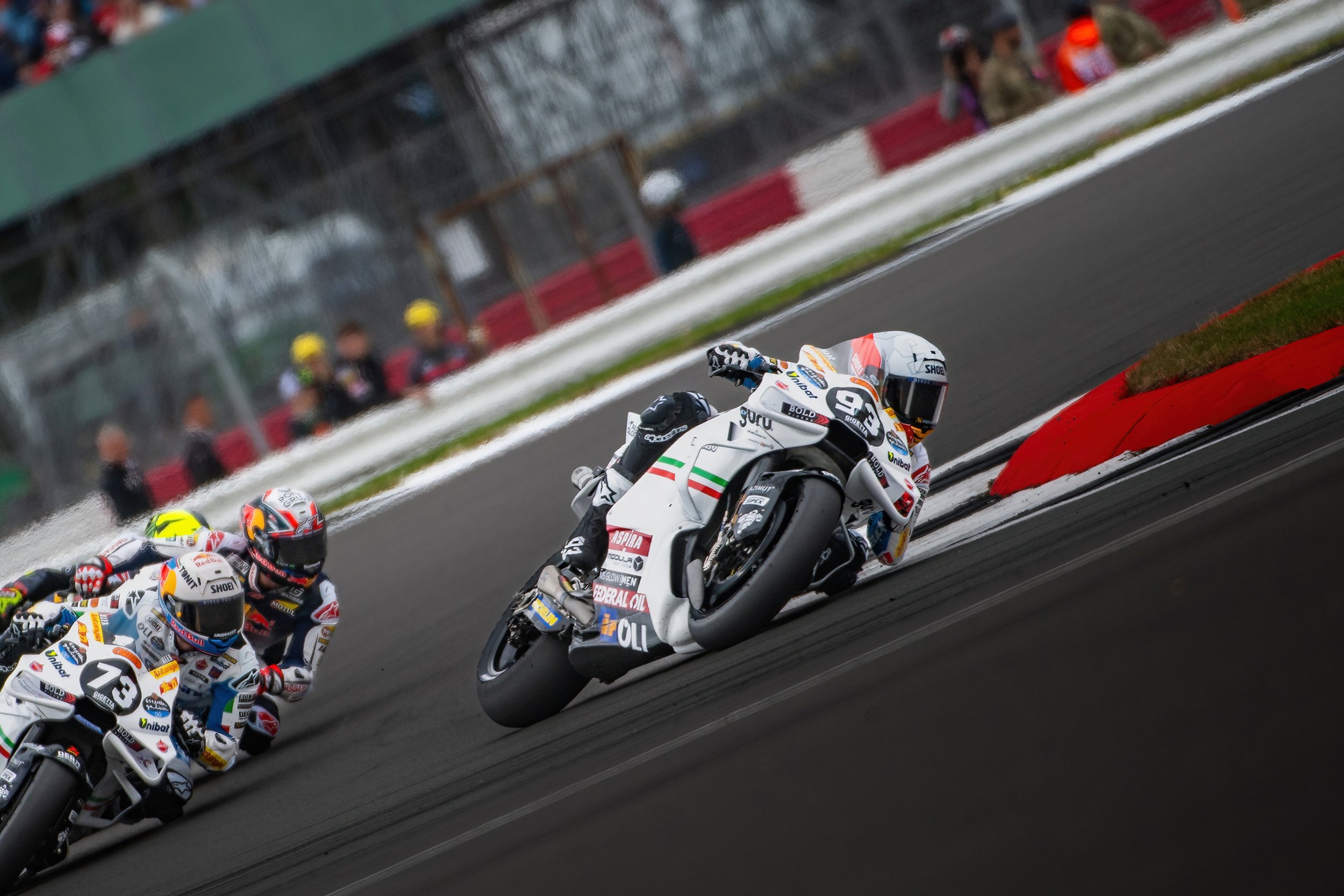 Race car riders leaning into a turn on a race track during a motorsport event.