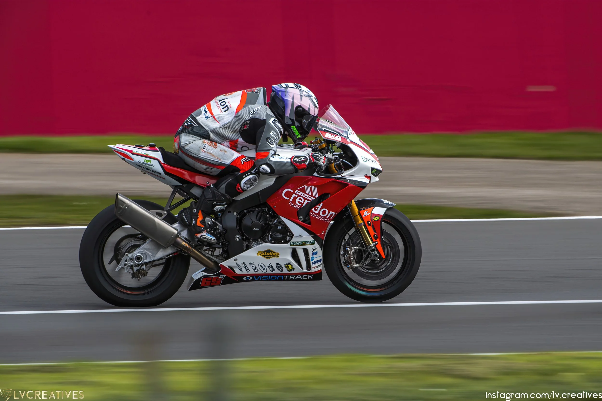 Motorcycle racer in full gear riding a red and white motorcycle on a race track with a blurred background.