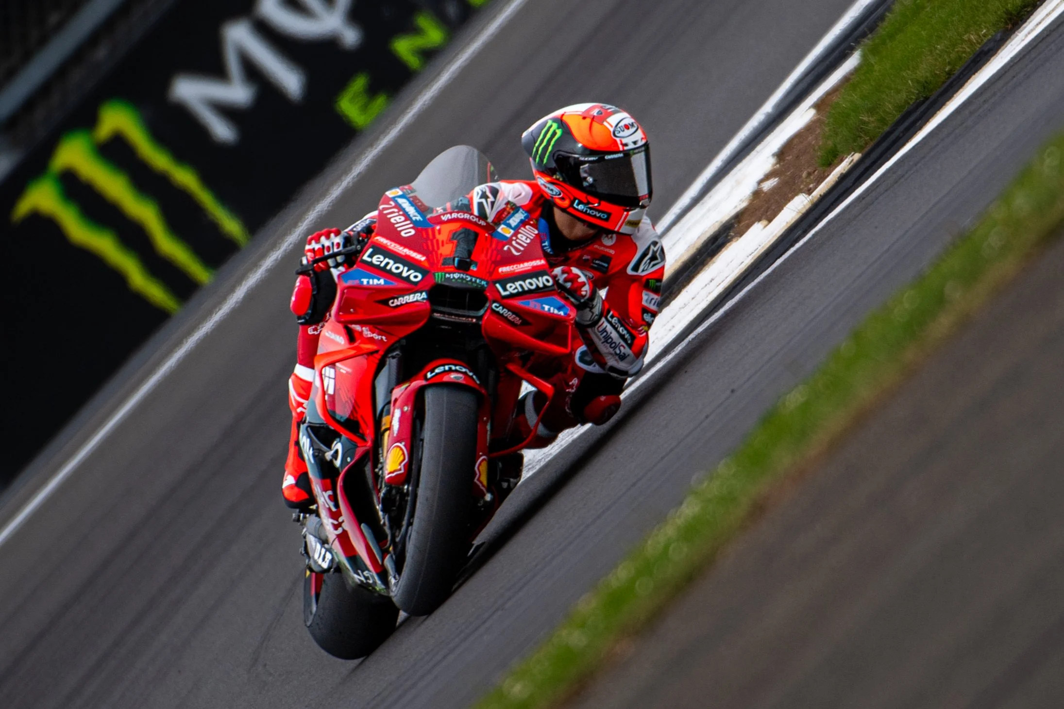 A professional motorcycle racer wearing a red racing suit and helmet, riding a red Ducati bike on a race track.