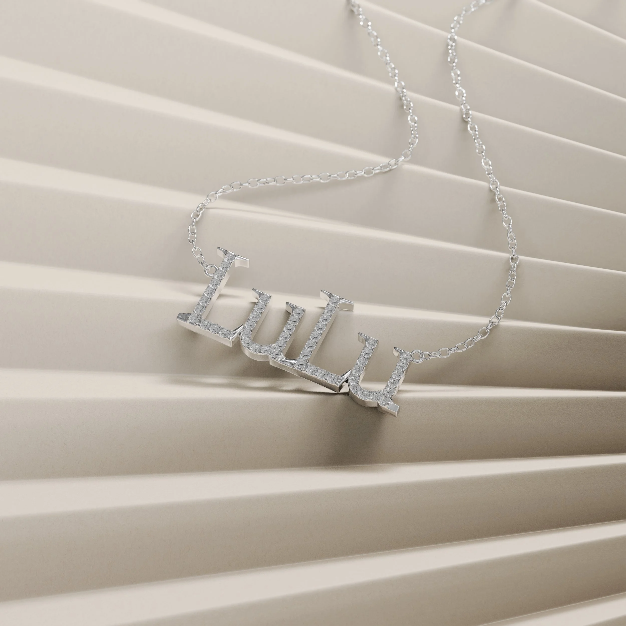 Silver necklace with the word "Lulu" spelled out in rhinestones, resting on a white textured surface.
