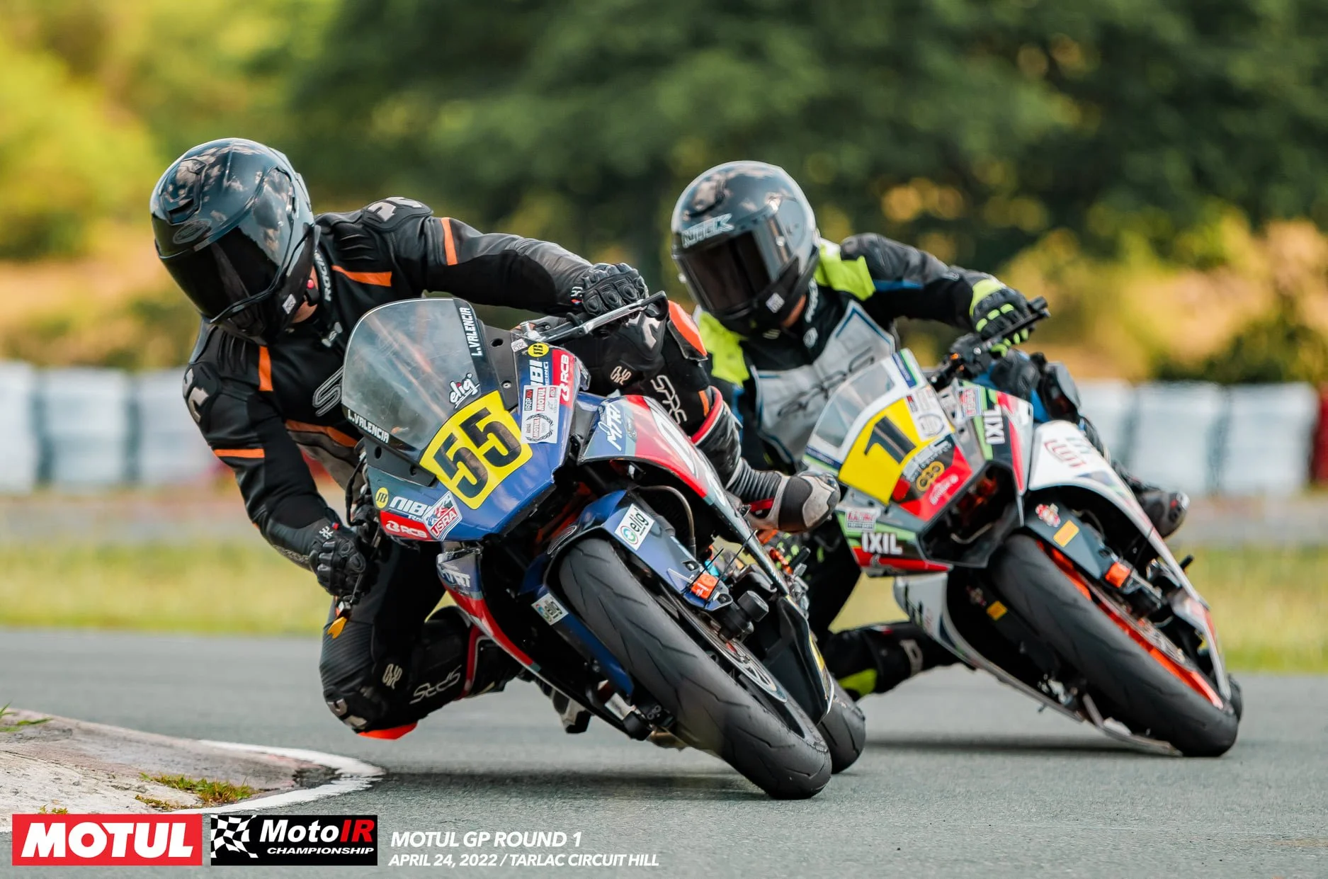 Lawrence Valencia and Carl Ferrer in an intense battle, leaning into a turn on a racetrack during a MotoIR Championship race.